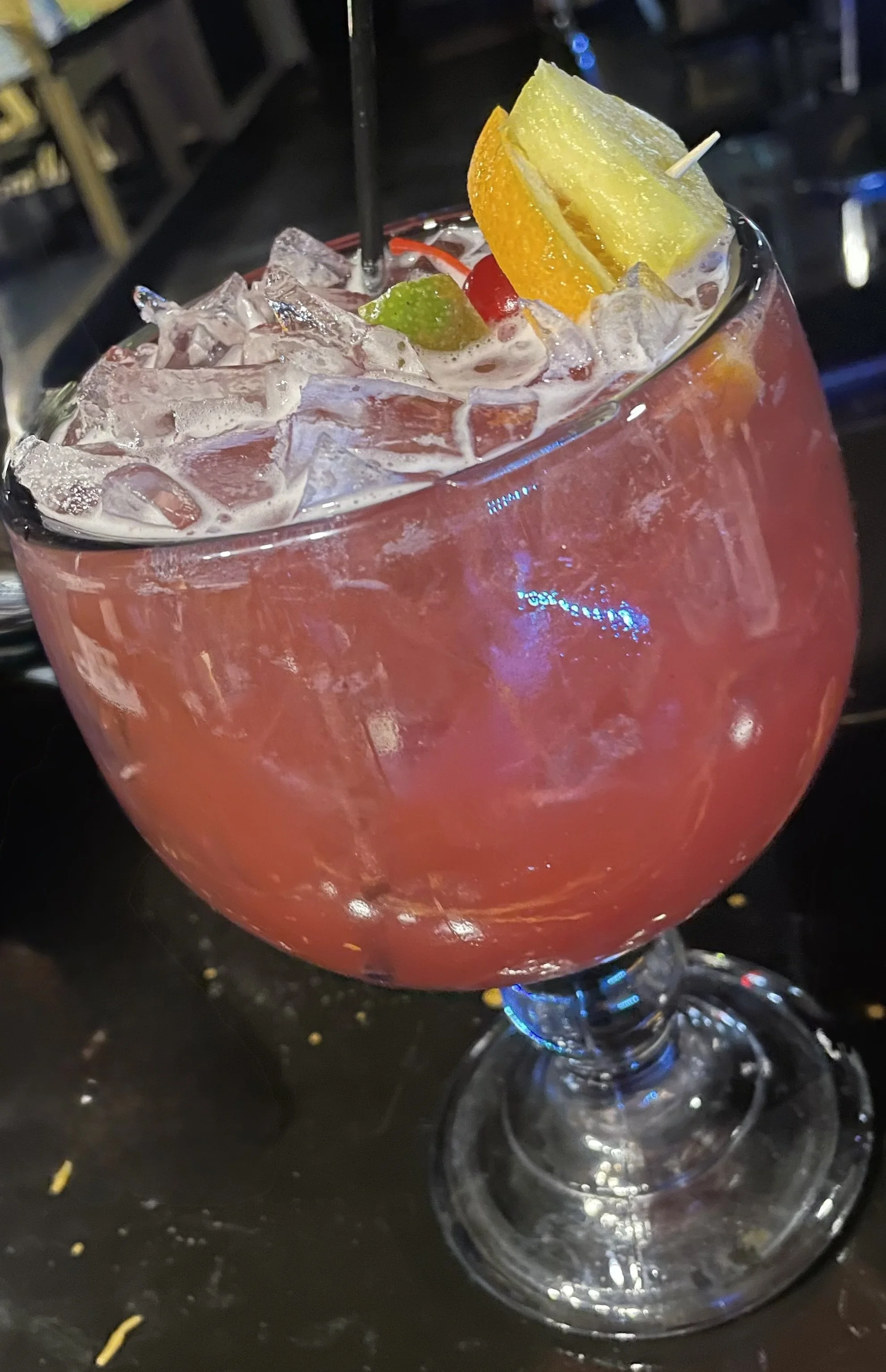 A large glass bowl filled with a pink cocktail topped with ice, an orange wedge, a pineapple wedge, a cherry, and a lime slice.