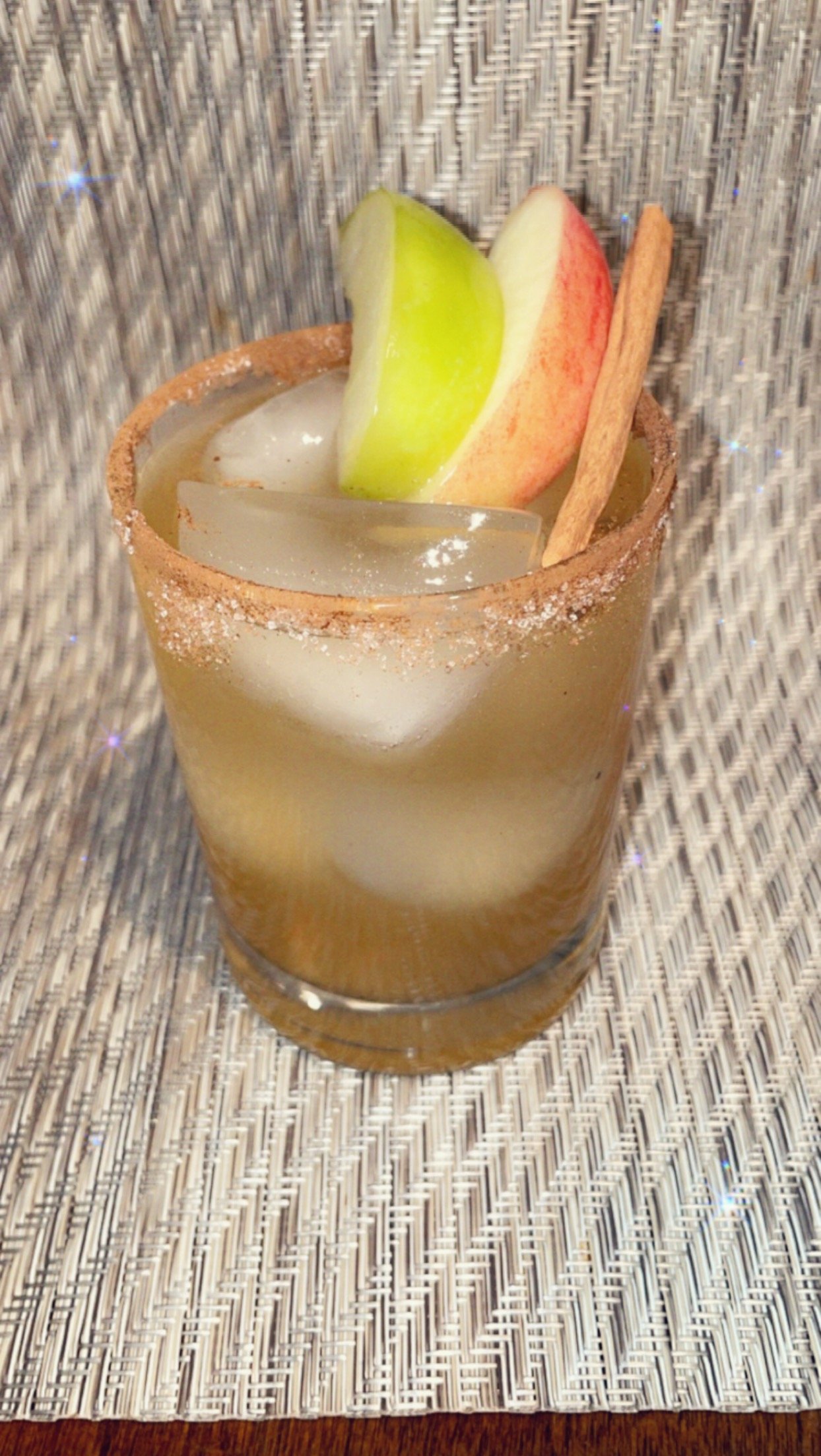 A cocktail glass with a salted rim, filled with ice, and garnished with apple slices and a cinnamon stick.