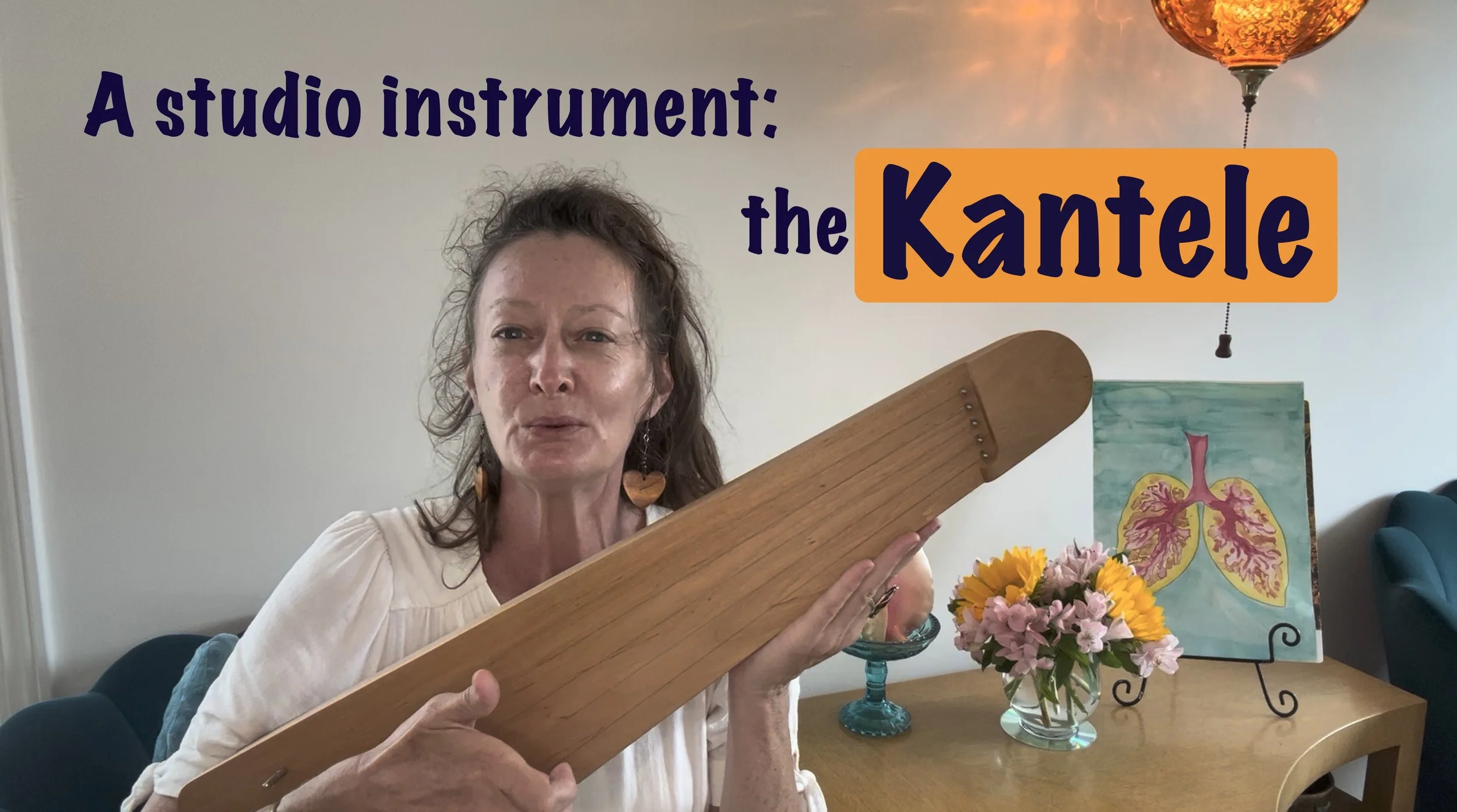A woman holding a wooden instrument with a salt shaker handle, standing in a room with a table that has flowers, a painting of lungs, and a ceiling fan in the background.