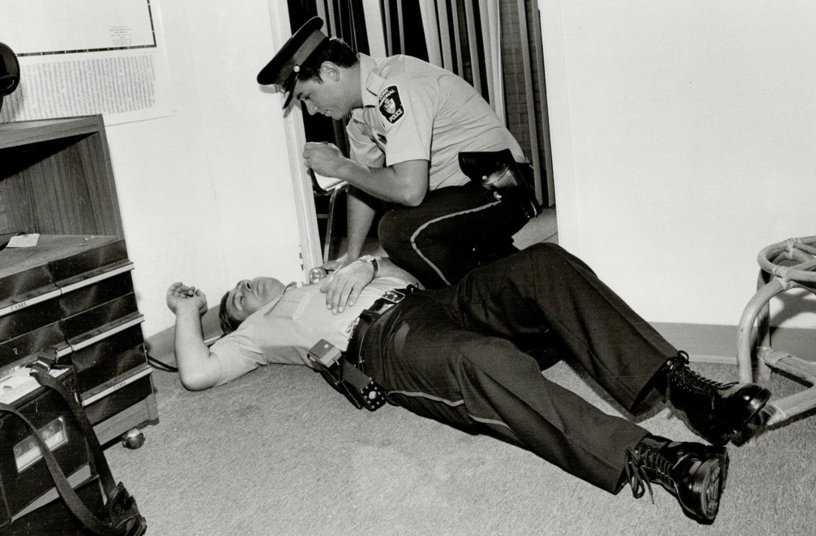 A police officer is kneeling next to a man lying on the floor, appearing unconscious.