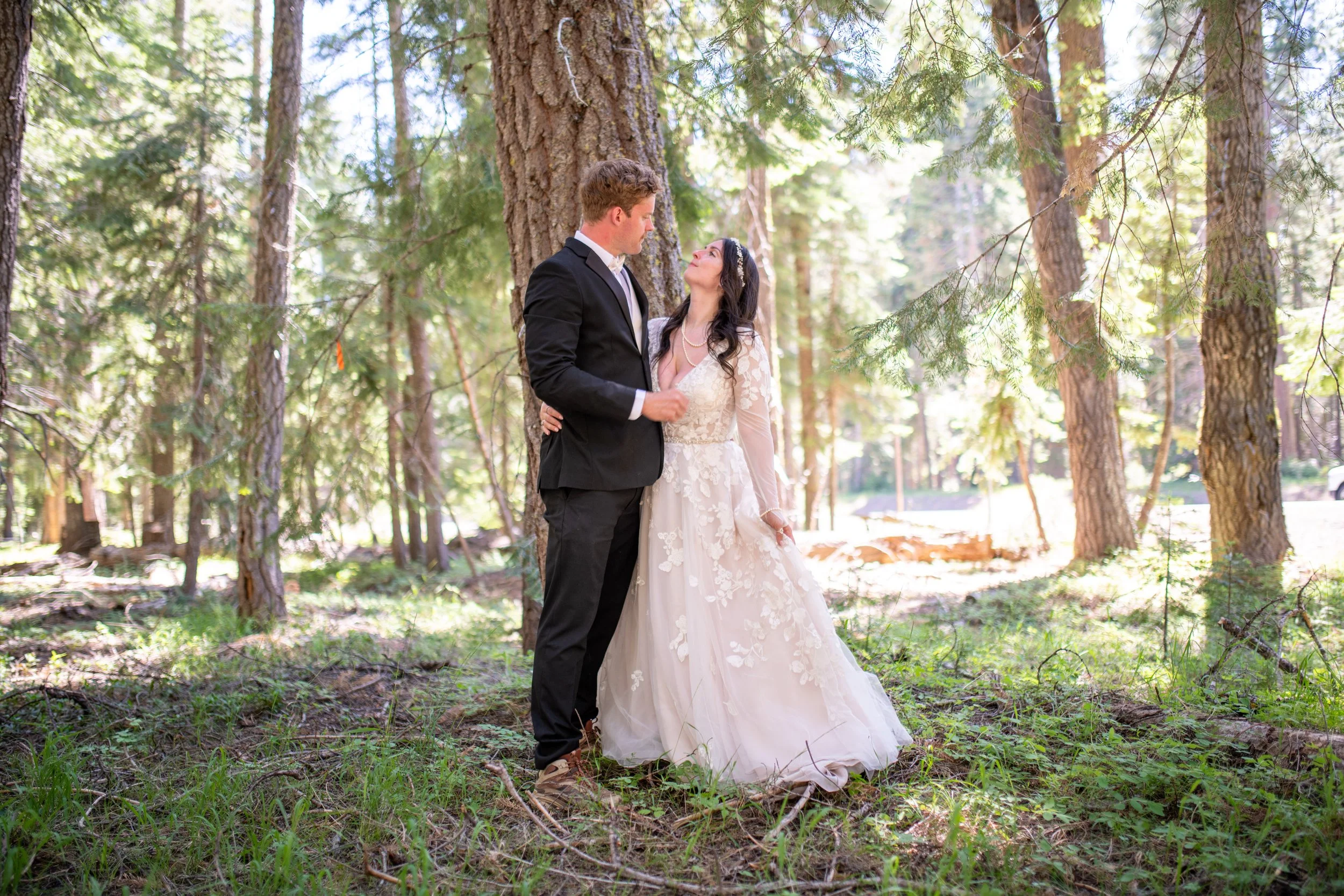 A bride and groom standing close together in a forest, gazing into each other's eyes during their wedding.