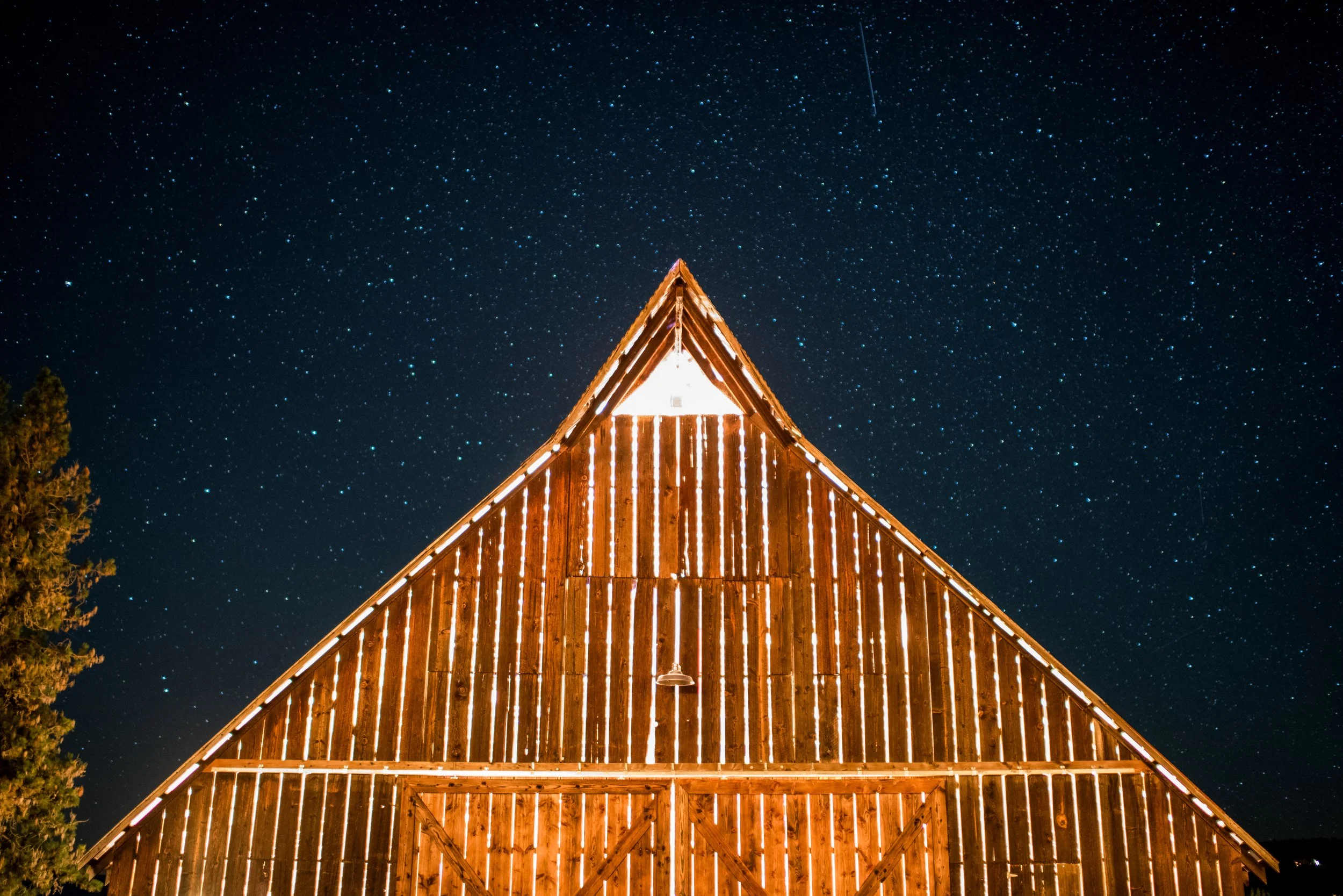 A wooden building with Christmas lights on its roof, set against a starry night sky with a visible shooting star.