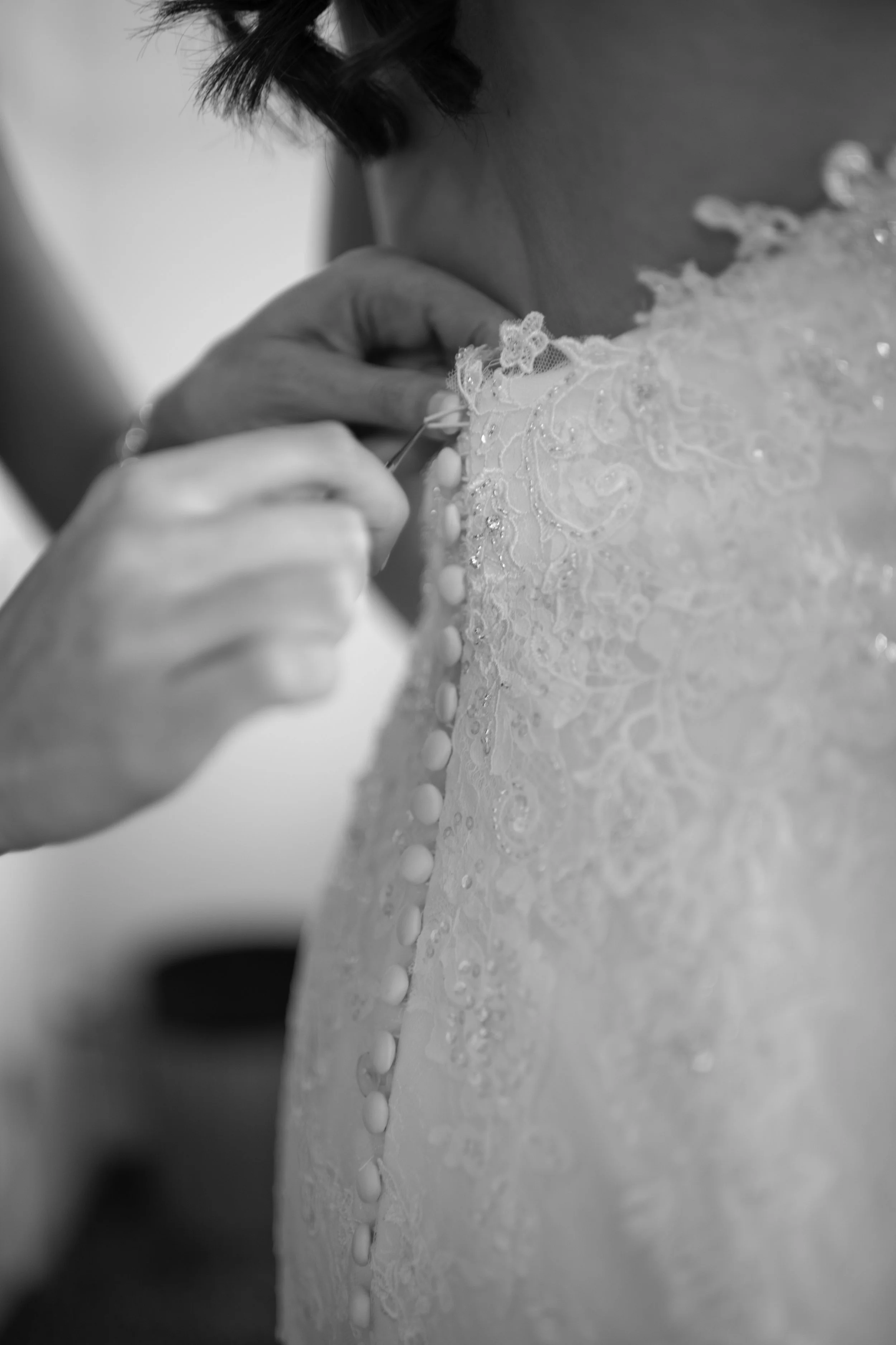 Close-up of a bride sewing or adjusting fabric on her wedding dress, showing detailed embroidery and buttons.