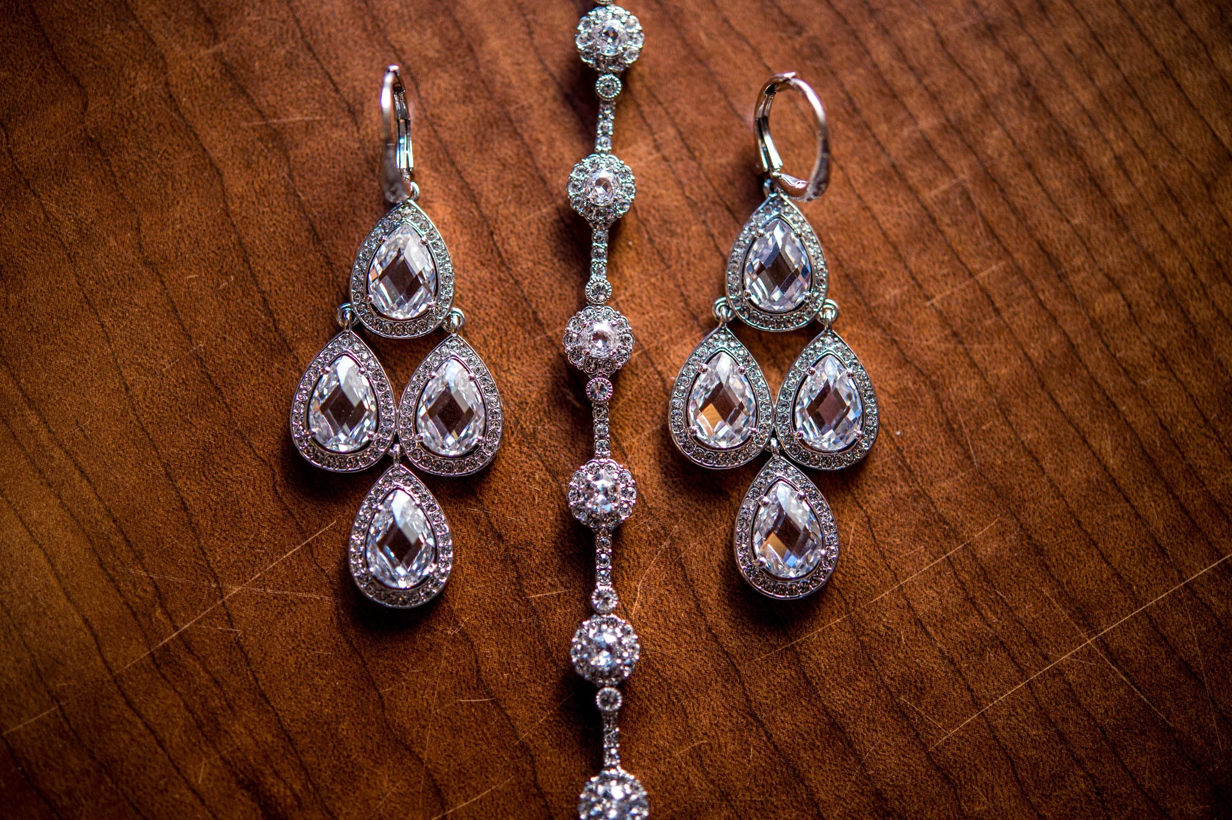 A set of silver jewelry including a pair of dangling earrings and a bracelet with clear, pear-shaped and round gemstones, arranged on a wooden surface.