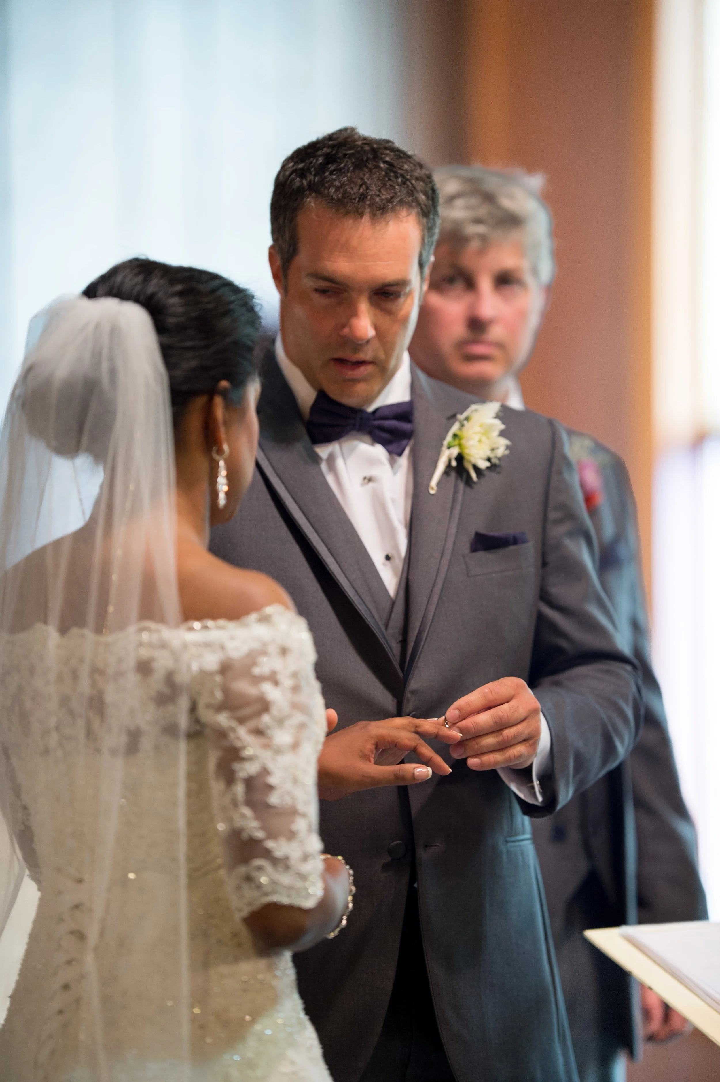 A bride and groom exchanging rings during a wedding ceremony, with officiant standing nearby.