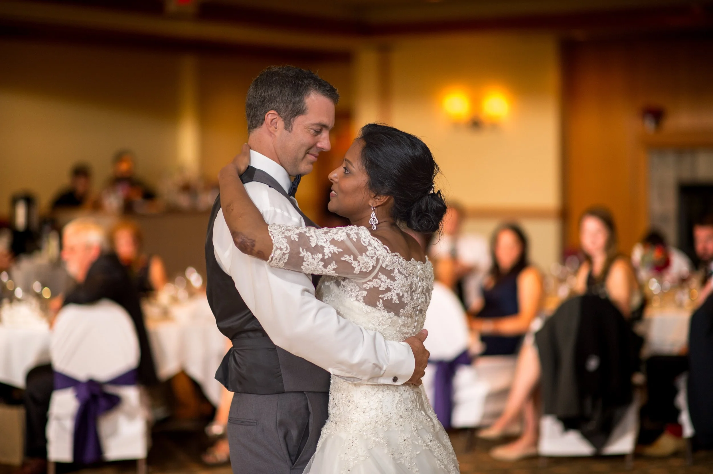 A bride and groom dancing closely at their wedding reception with guests in the background.