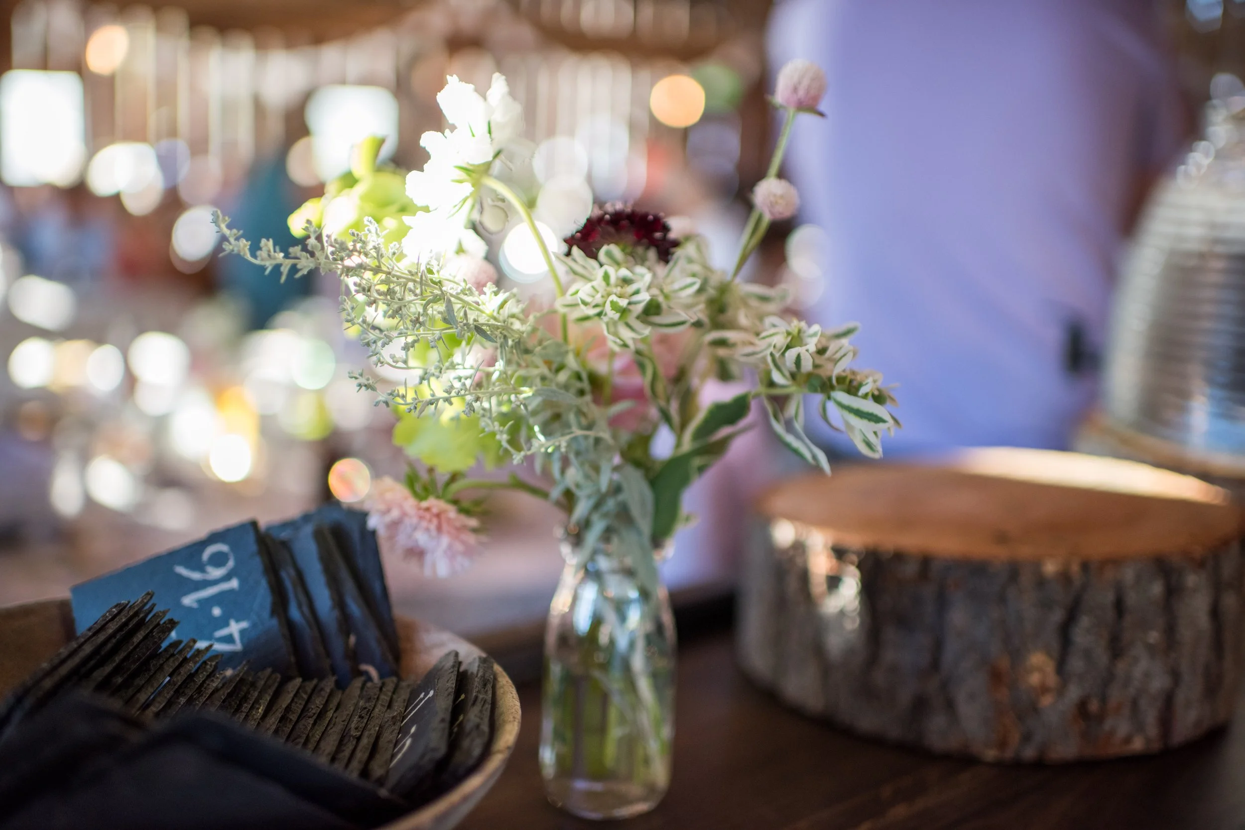 A glass vase filled with white and pink flowers on a wooden table with a blurred background.