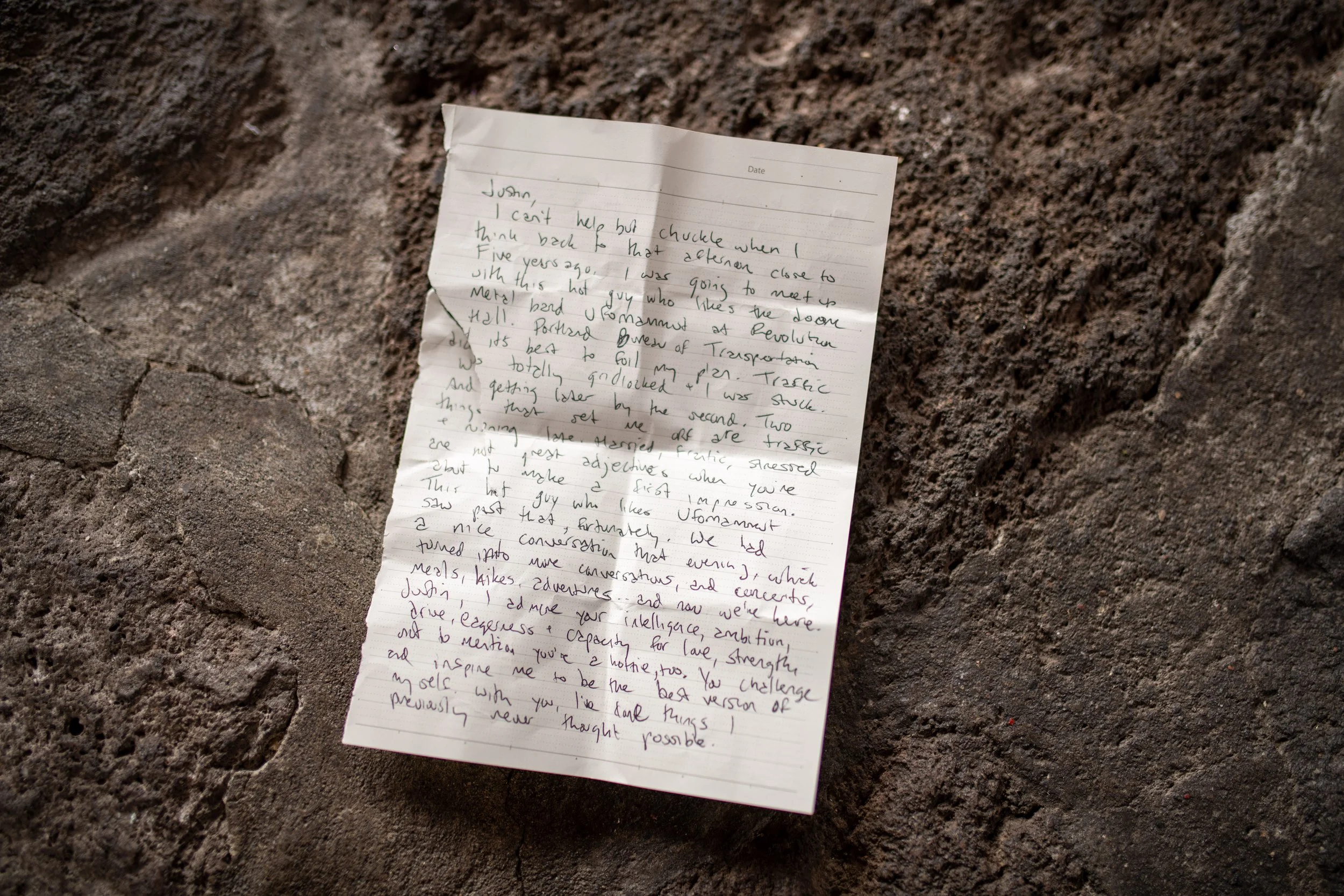 A handwritten note on a piece of paper resting on a dirt or soil surface.