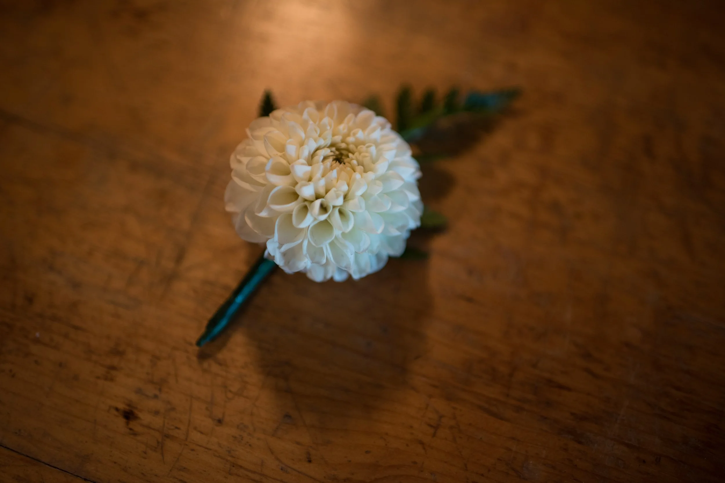 A white artificial flower with green leaves on a wooden surface.