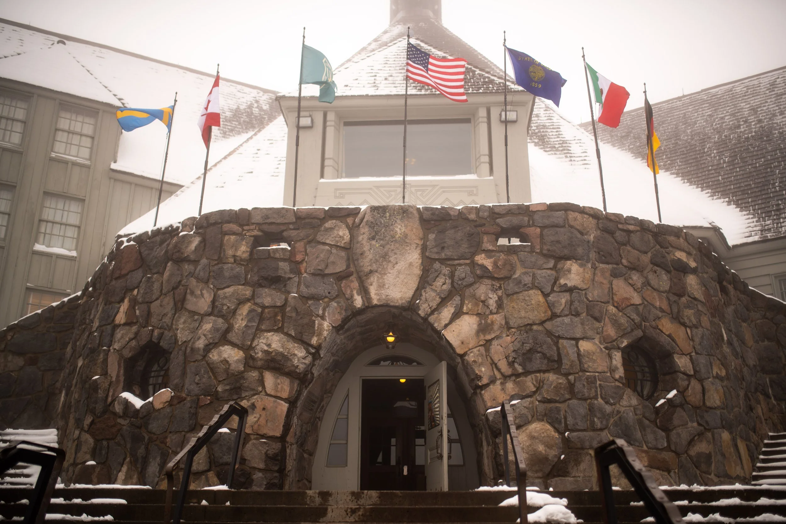 Entrance of a building with a stone archway and flags, including the United States flag, flying in snowy weather.
