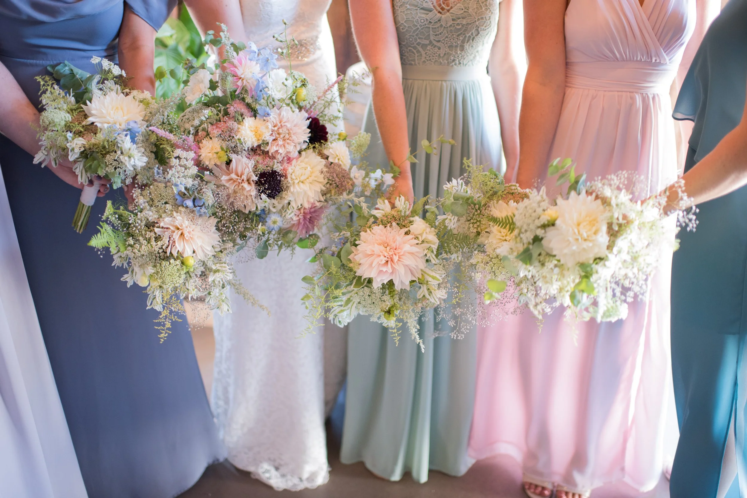 Group of women in pastel-colored dresses holding bouquets of flowers at a wedding or formal event.