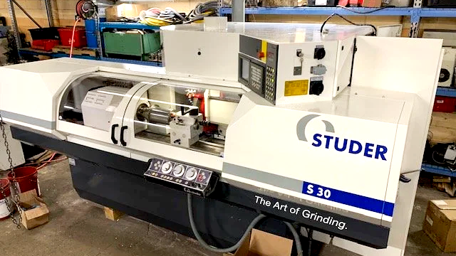 A Studer S30 cylindrical grinding machine in a workshop, with controls and a workpiece holder visible.