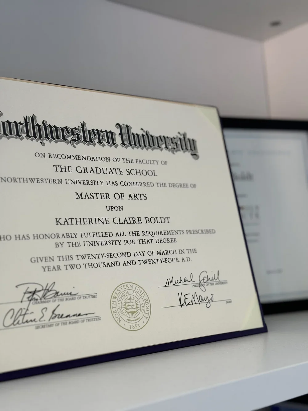 Northwestern University graduation certificate for Katherine Claire Boldt, conferring a Master of Arts degree, signed by university officials, with the university's seal, resting on a white surface.