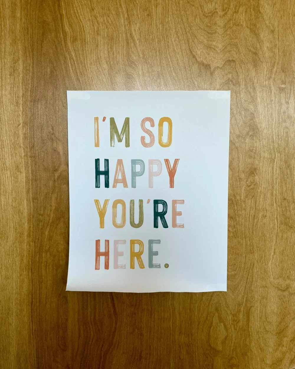 Colorful sign on a wooden door that reads, 'I'M SO HAPPY YOU'RE HERE.' in multicolored capital letters.
