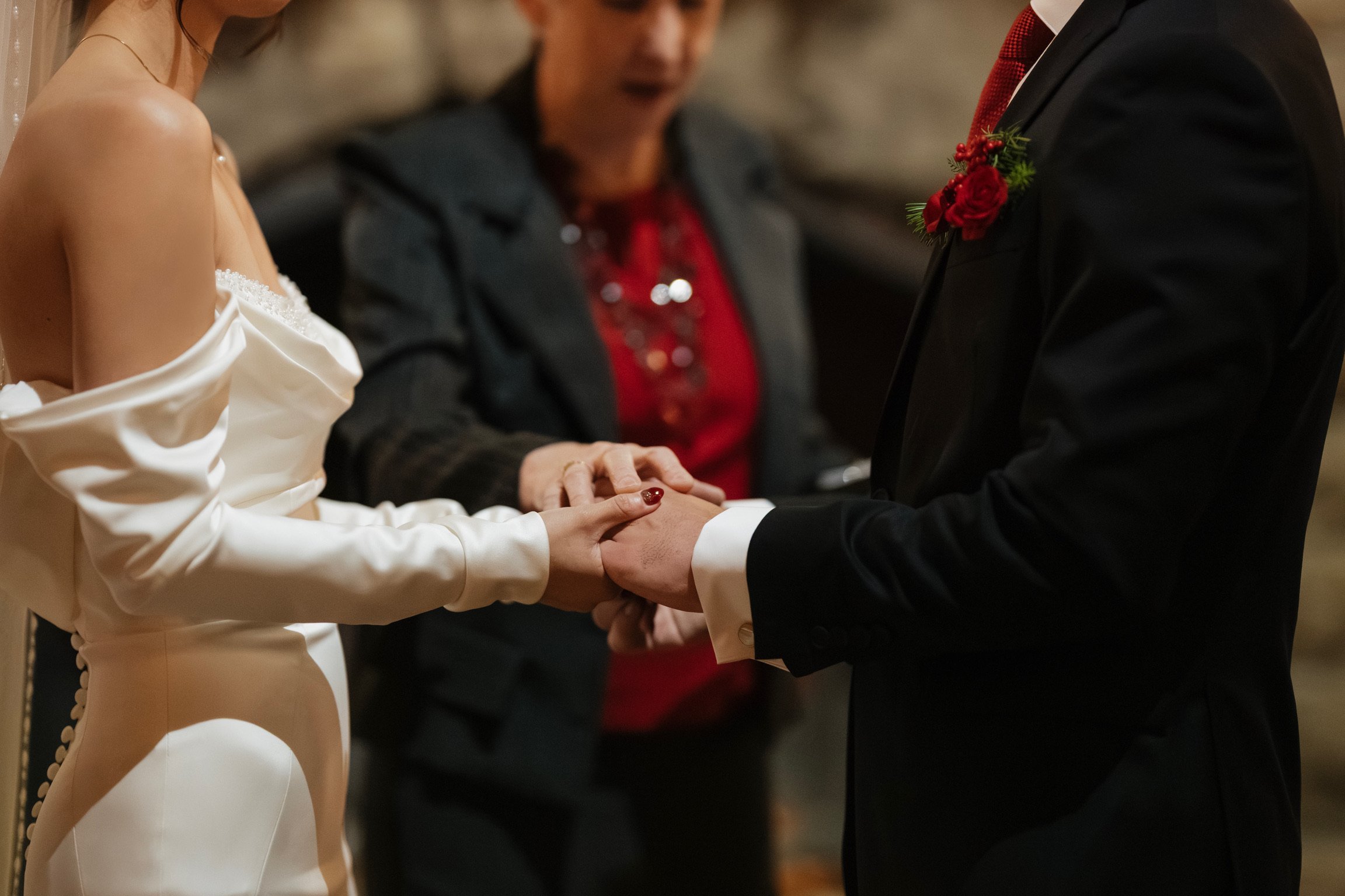 Close-up of a wedding ceremony showing a bride and groom holding hands and a woman officiant between them, with a blurred background.