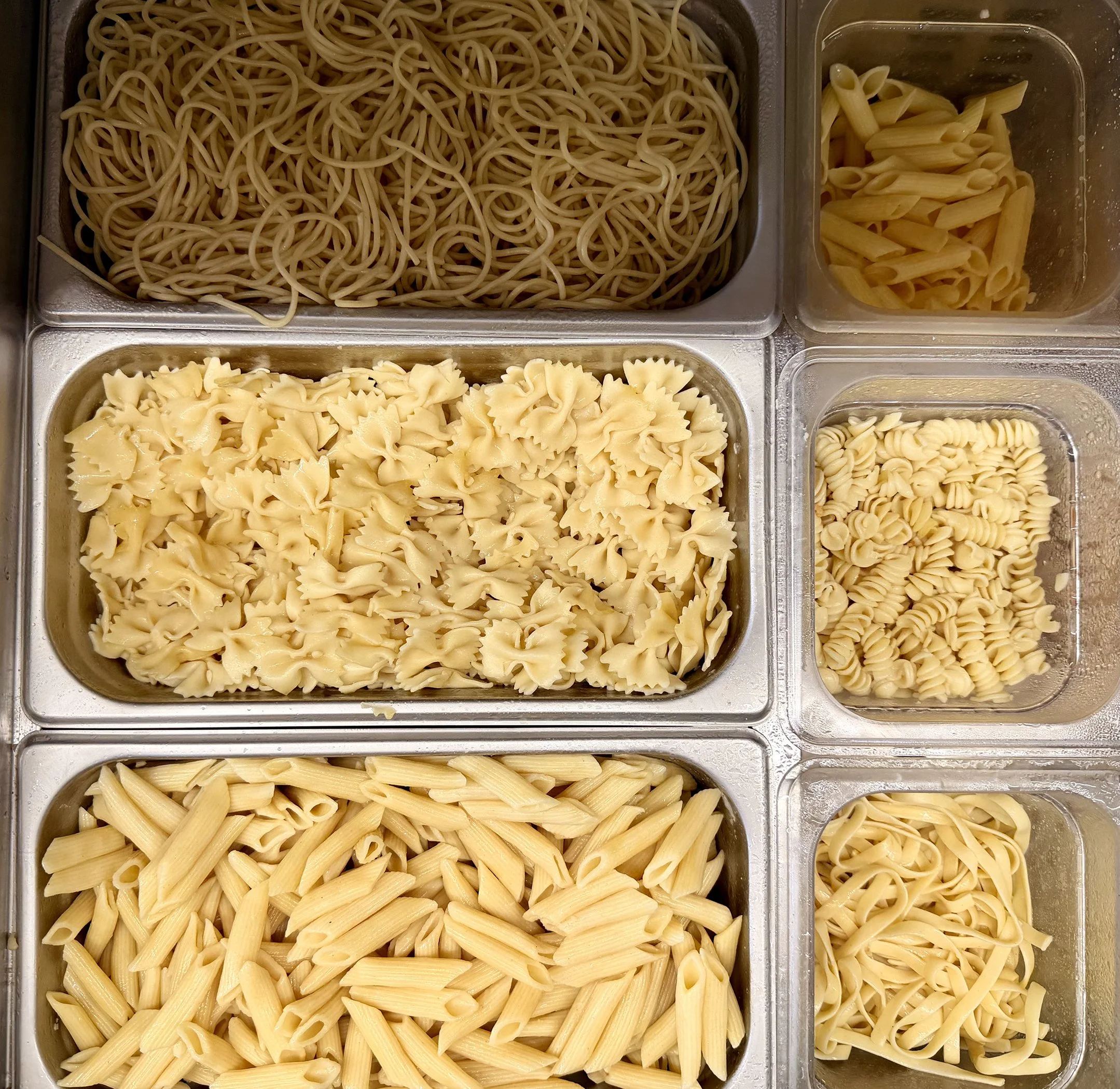Tray of different types of uncooked pasta, including spaghetti, penne, fusilli, and farfalle.