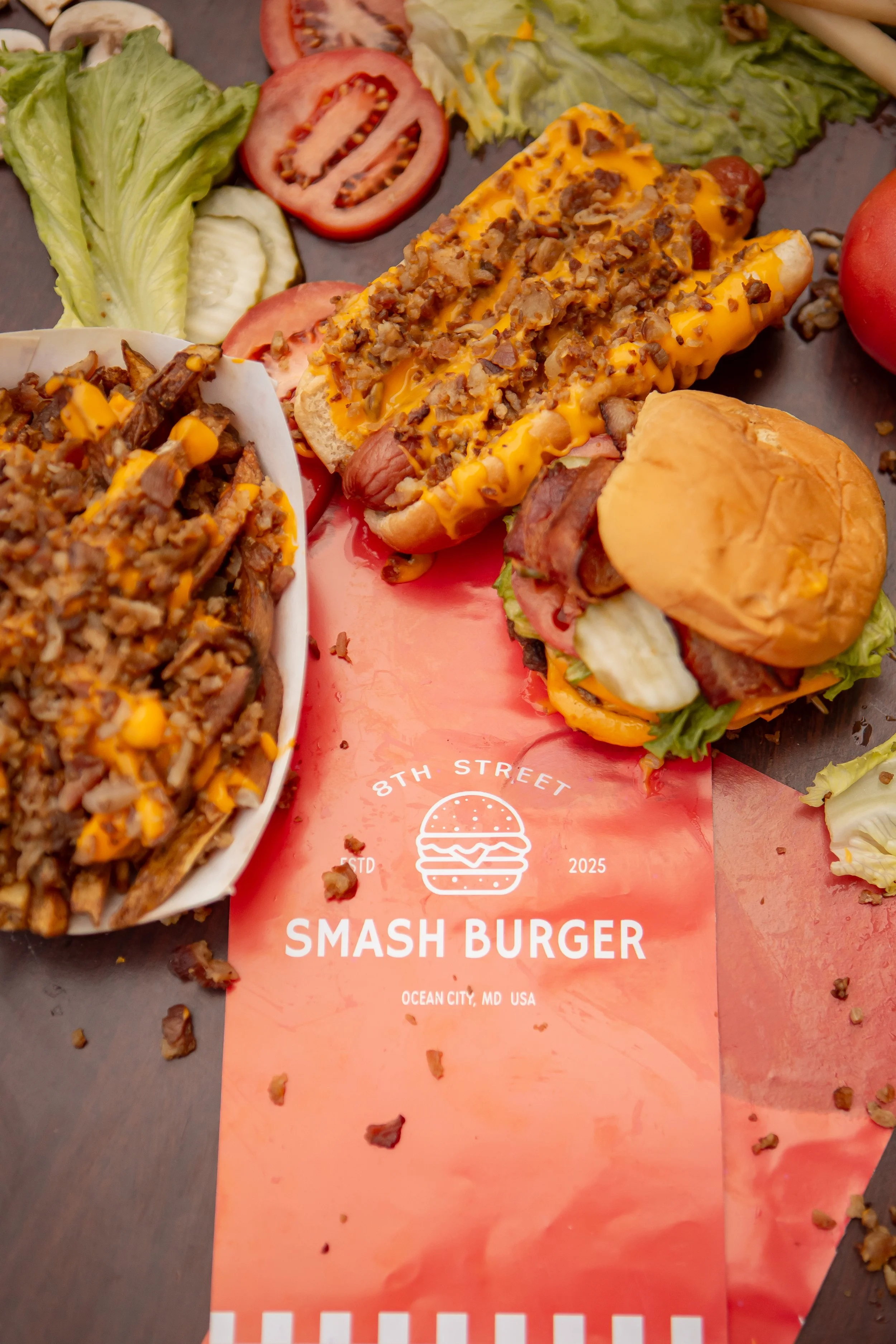 Close-up of a Smash Burger advertisement on a pink paper with a burger, fries, ketchup, lettuce, tomato, and a toasted bun surrounded by scattered bits of food.