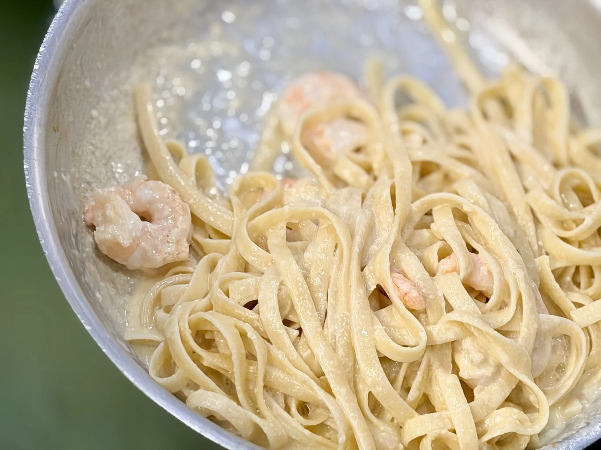 Close-up of creamy fettuccine pasta with shrimp in a metallic container.