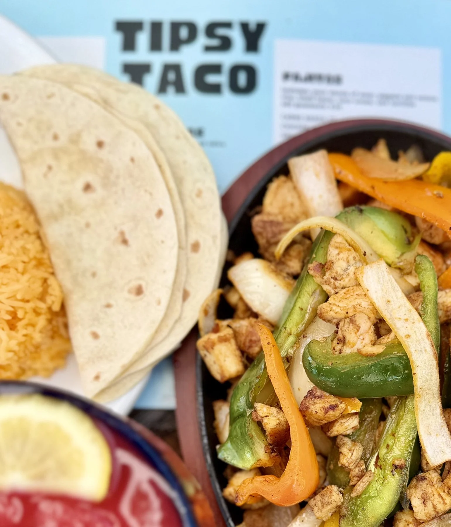 A close-up of a Taco Bell Tipsy Taco with seasoned ground chicken, sautéed bell peppers, and shredded cheese, accompanied by a side of Mexican rice and a taco shell.