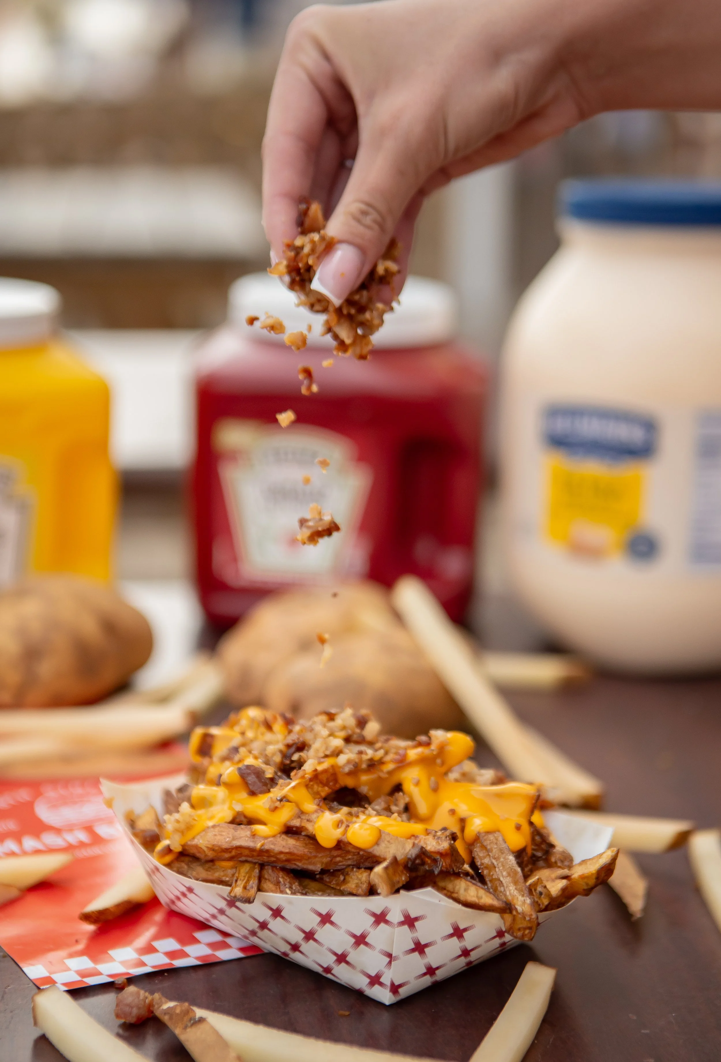 Close-up of a serving of loaded nachos topped with shredded cheese, ground beef, and chopped toppings, with condiments and jars in the background.
