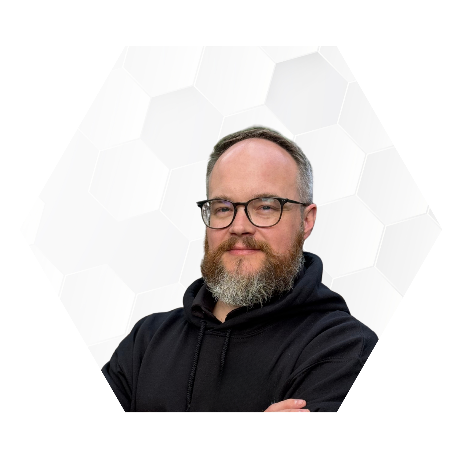 A man with glasses, a beard, and a mustache wearing a black hoodie, standing against a background with light gray hexagonal patterns.
