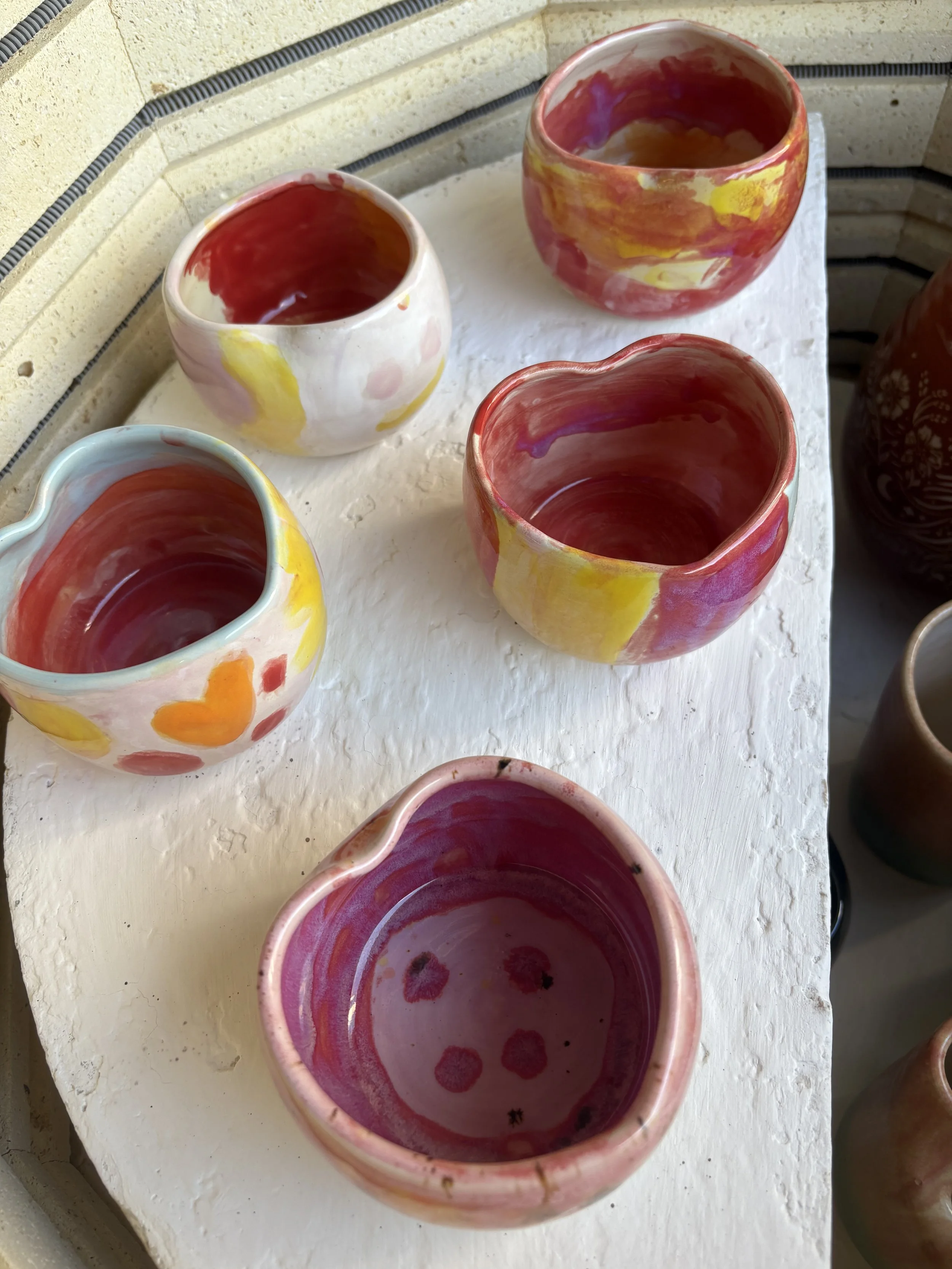 Colorful handmade ceramic bowls with various patterns and colors, displayed on a white surface.