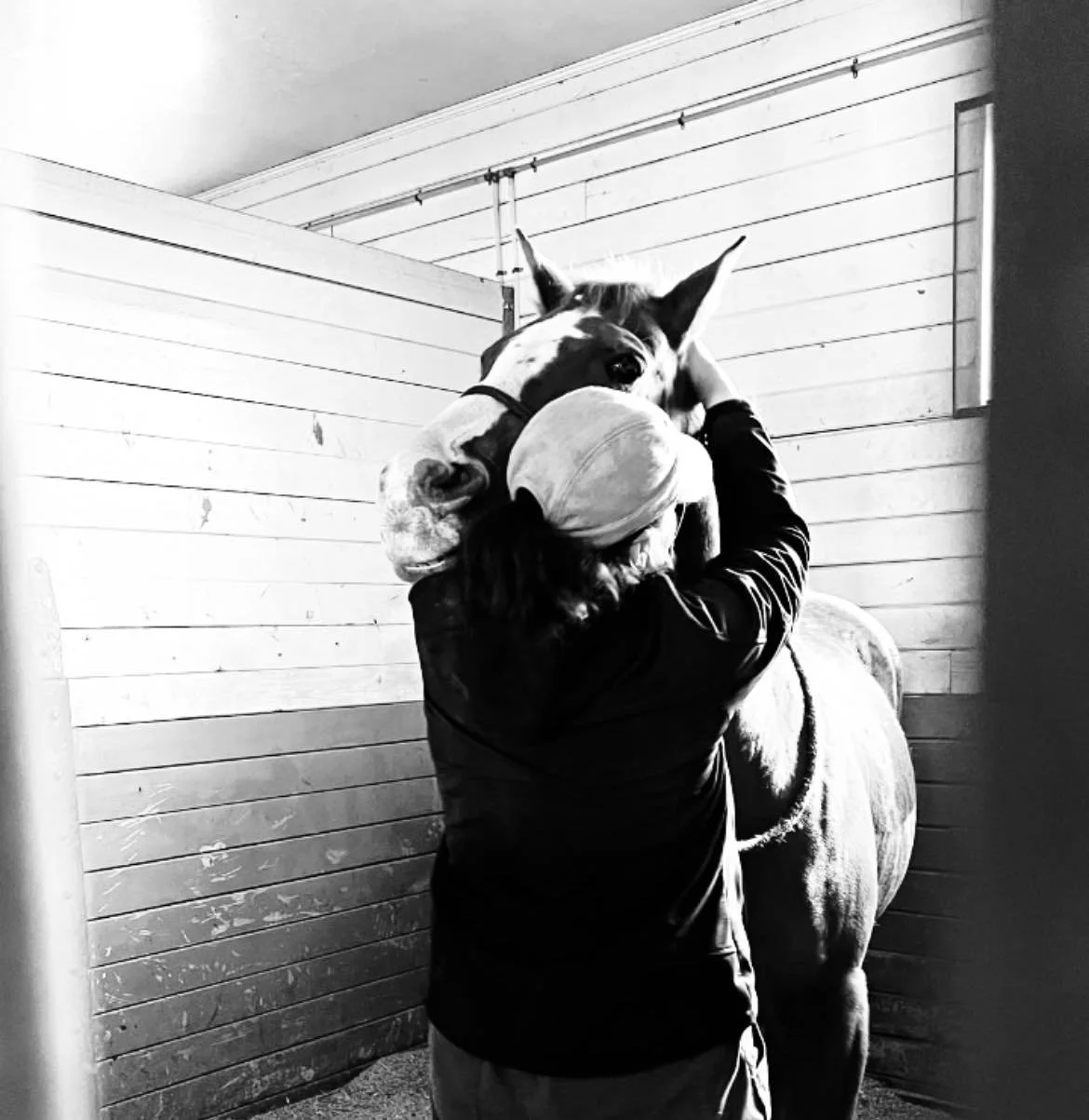 Person hugging a horse in a barn, black and white photograph