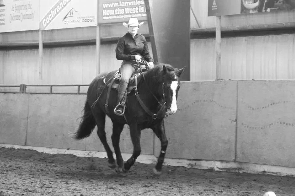 A person wearing a cowboy hat and dark clothing riding a horse in an indoor arena.