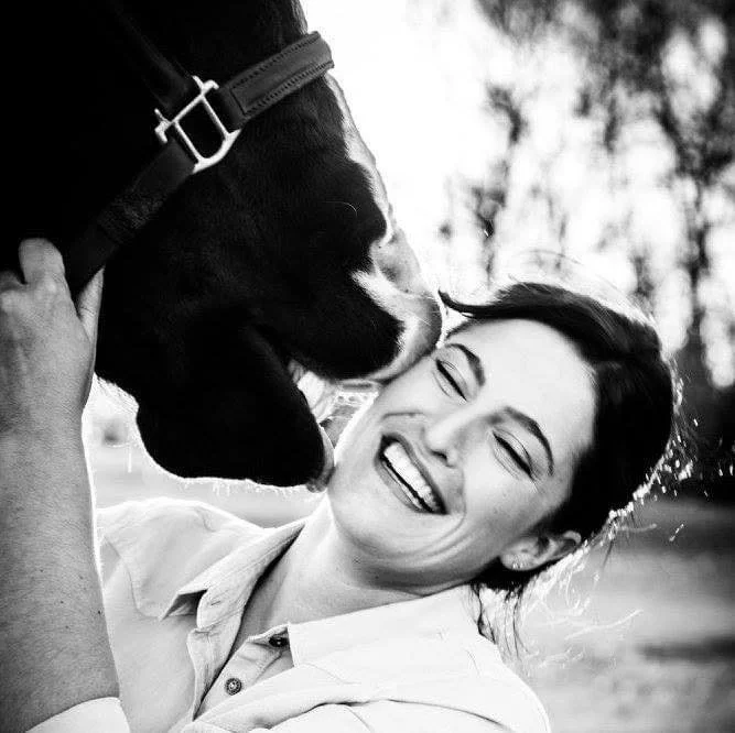 A woman smiling and laughing as a dog kisses her face outdoors.