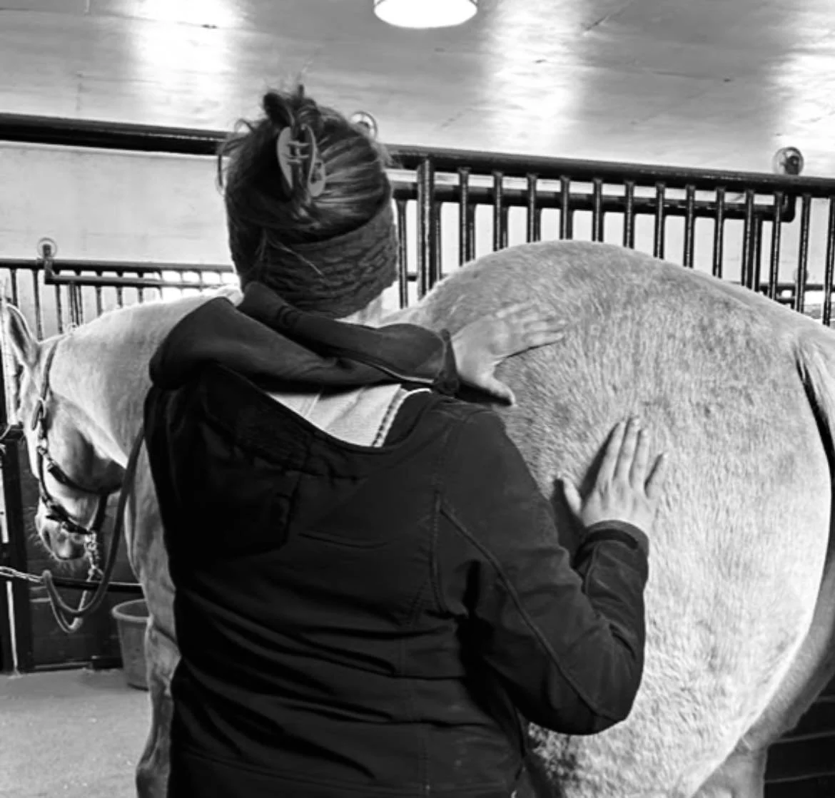 A person petting a horse in a stable, captured in black and white.