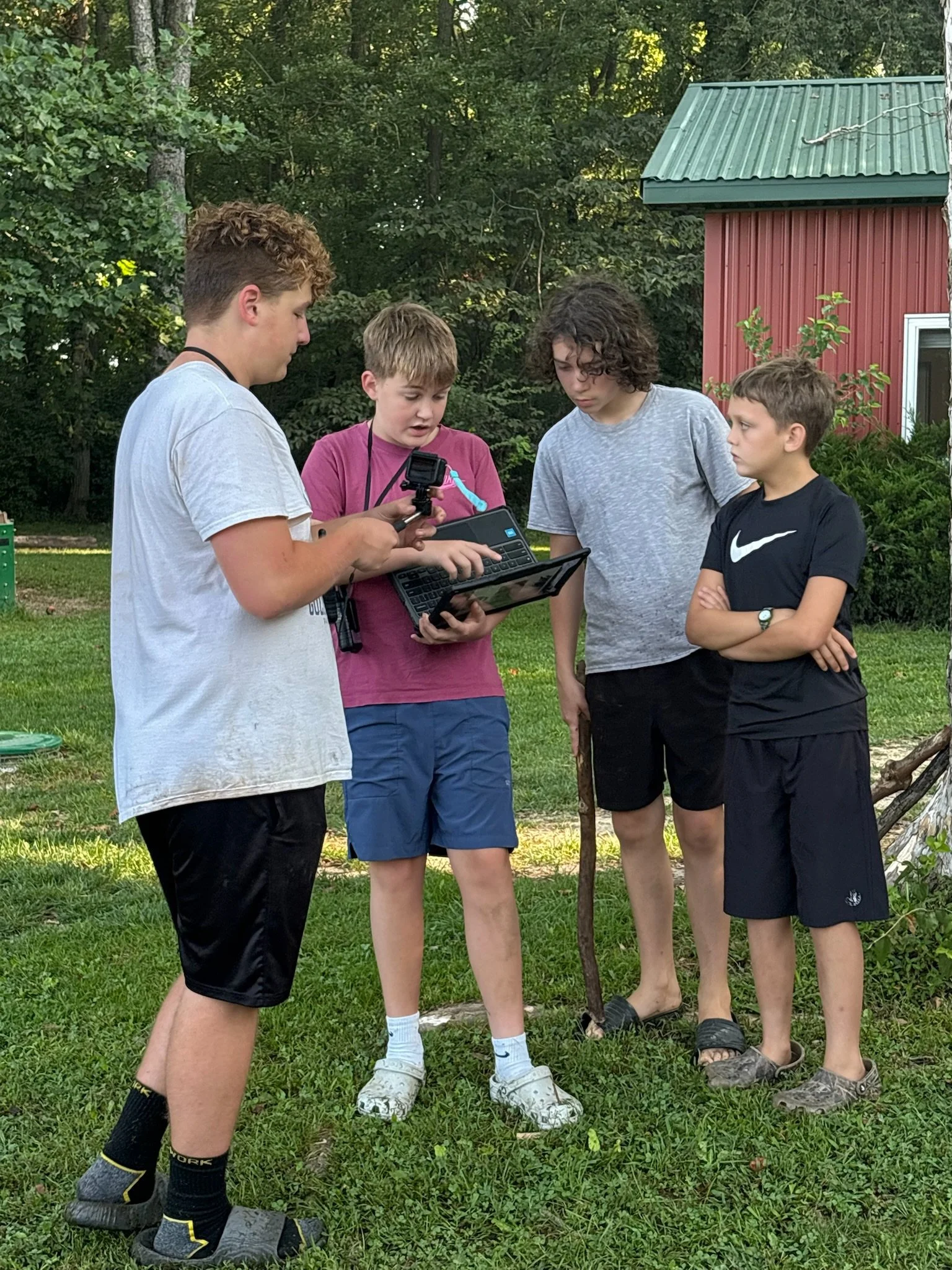 Four students work together outdoors with a laptop, camera, and other technology during a group project.