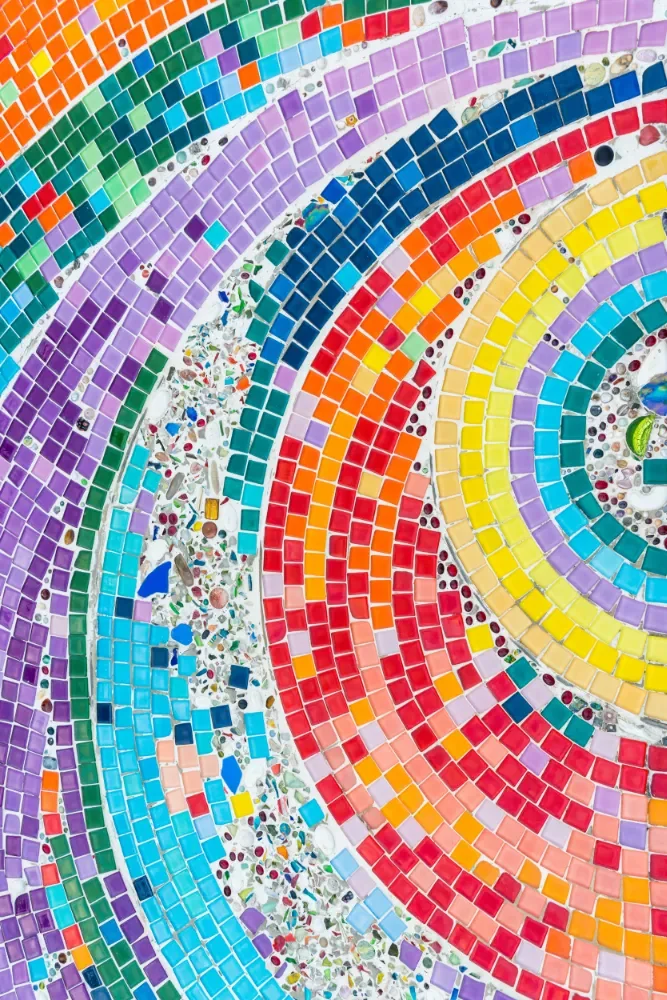Close-up view of a colorful mosaic made of small square tiles and glass pieces arranged in spiral patterns.