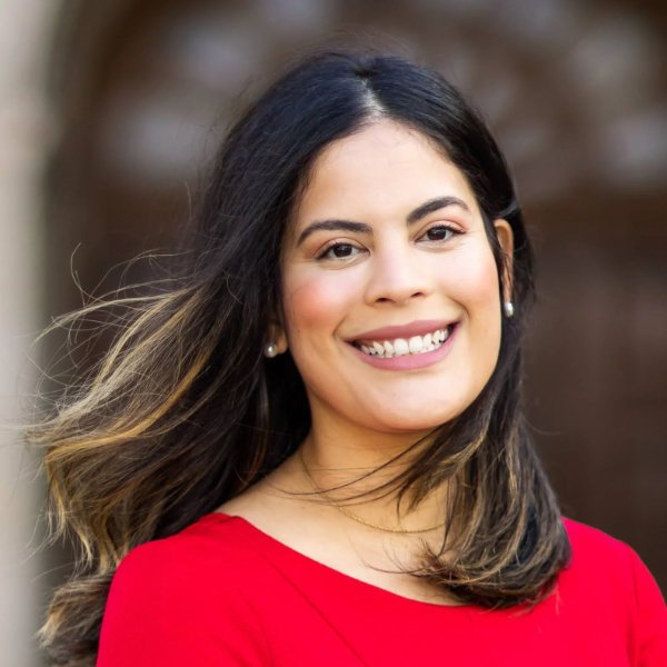 Therapist Liz Davila-Ferrall long dark hair, smiling, wearing a red top, outdoors with blurred background.
