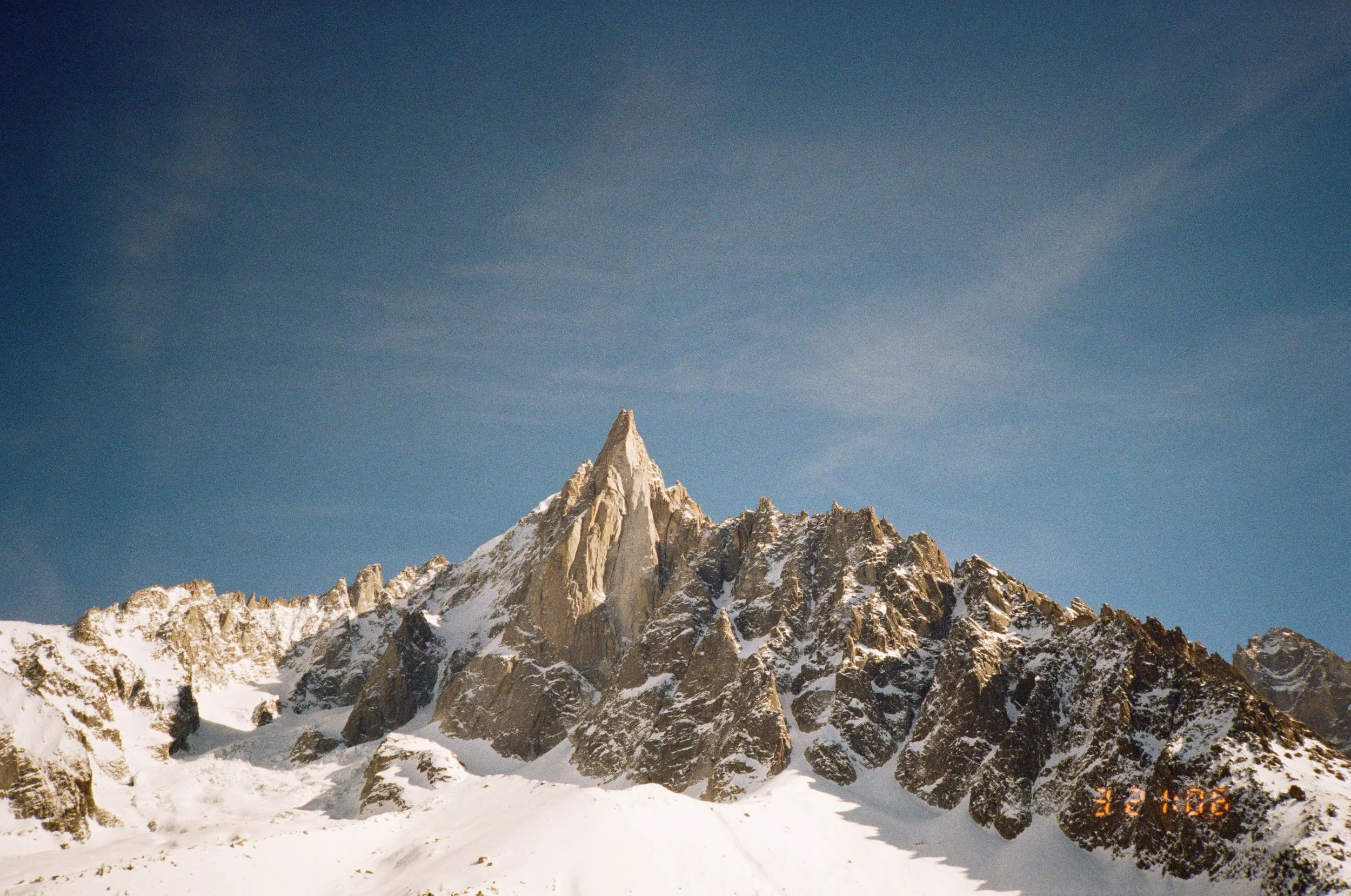 Snow-covered jagged mountain peaks under a cloudy blue sky.