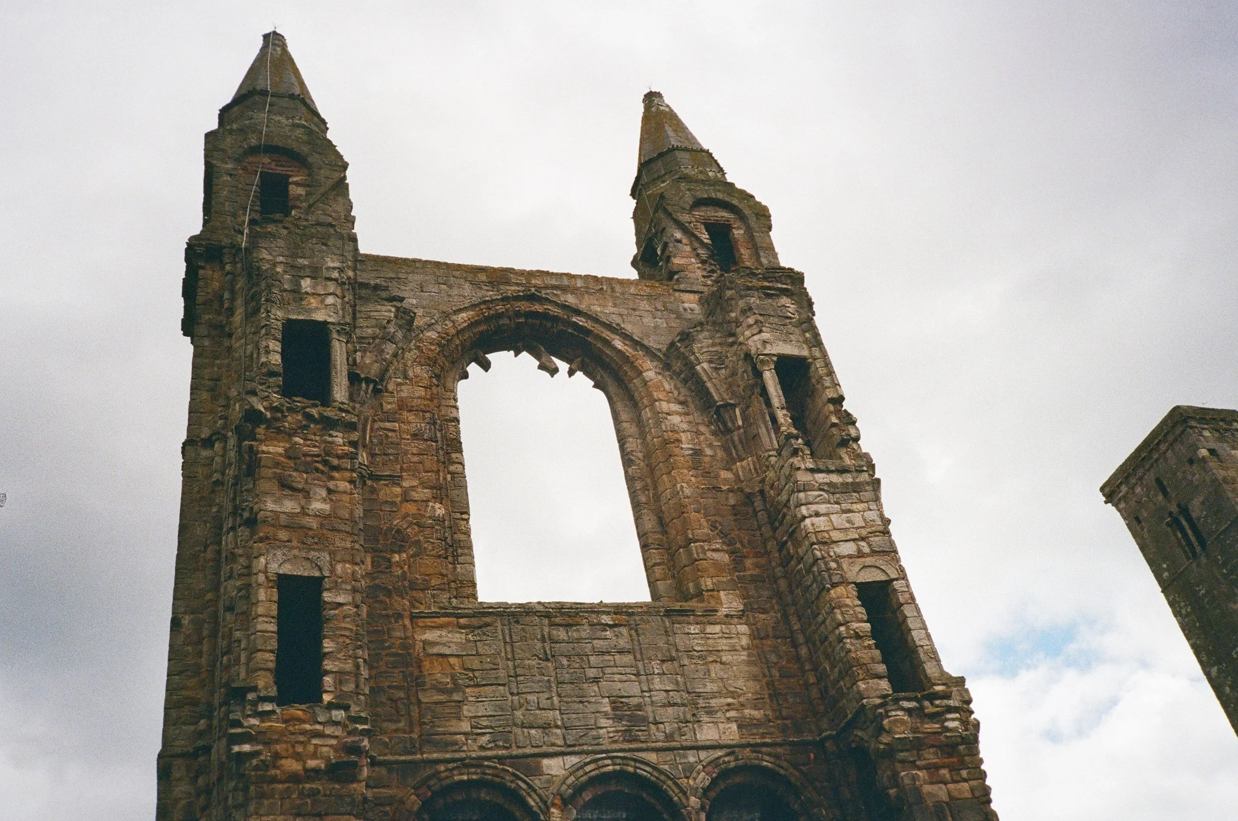 Ancient stone church ruins with two tall towers and a large, arched window in the center under a cloudy sky.