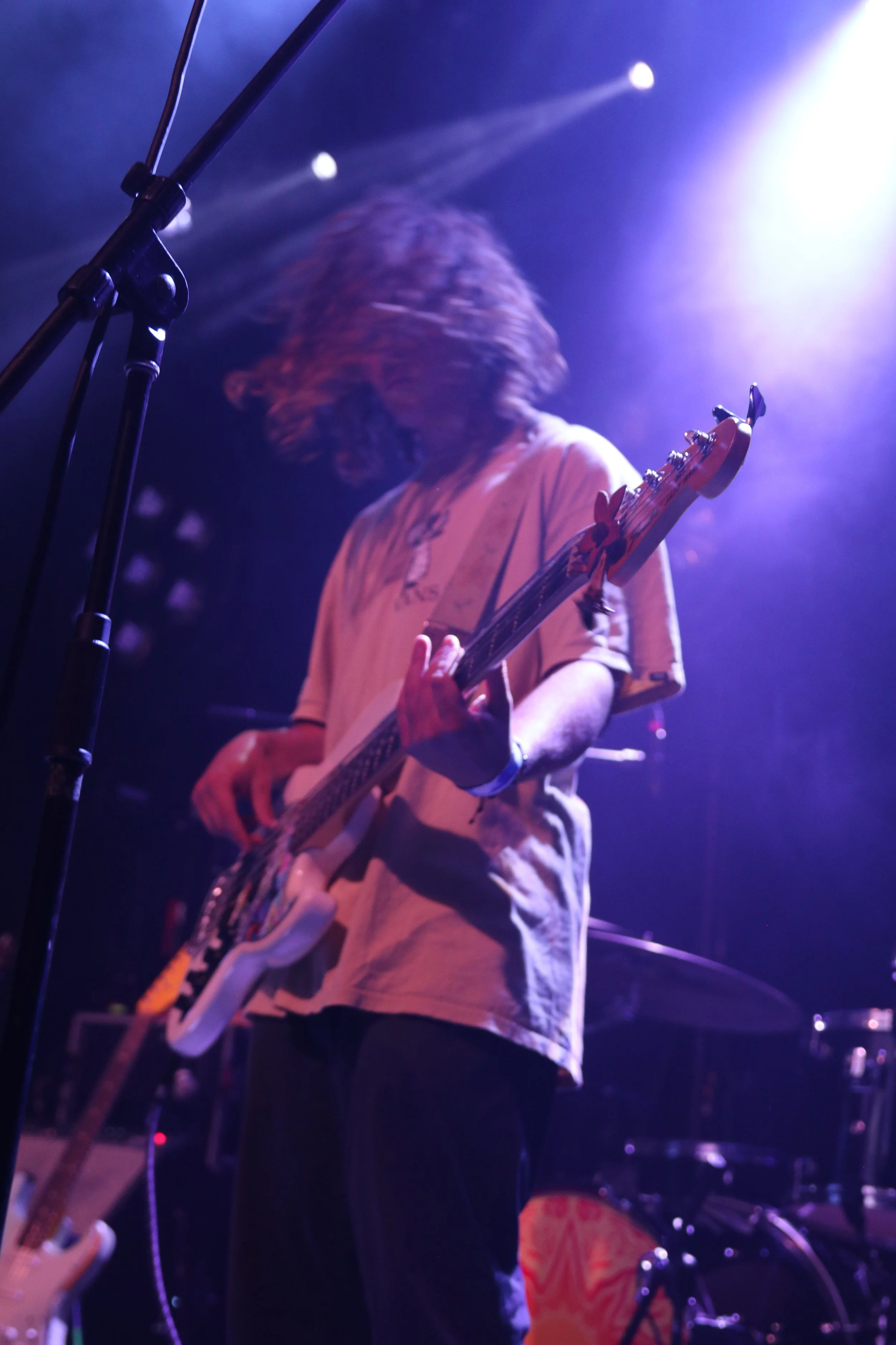 Musician playing bass guitar on stage with purple lighting.