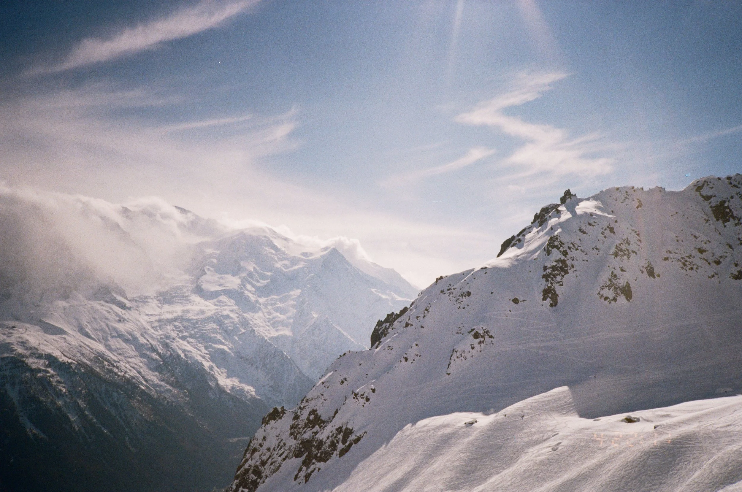 Snow-covered mountain range with clear skies and clouds in the background.