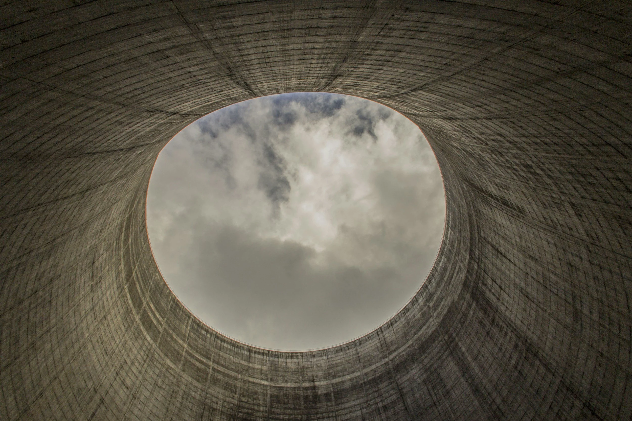Looking up through a tall cylindrical concrete structure with an opening at the top showing a cloudy sky.