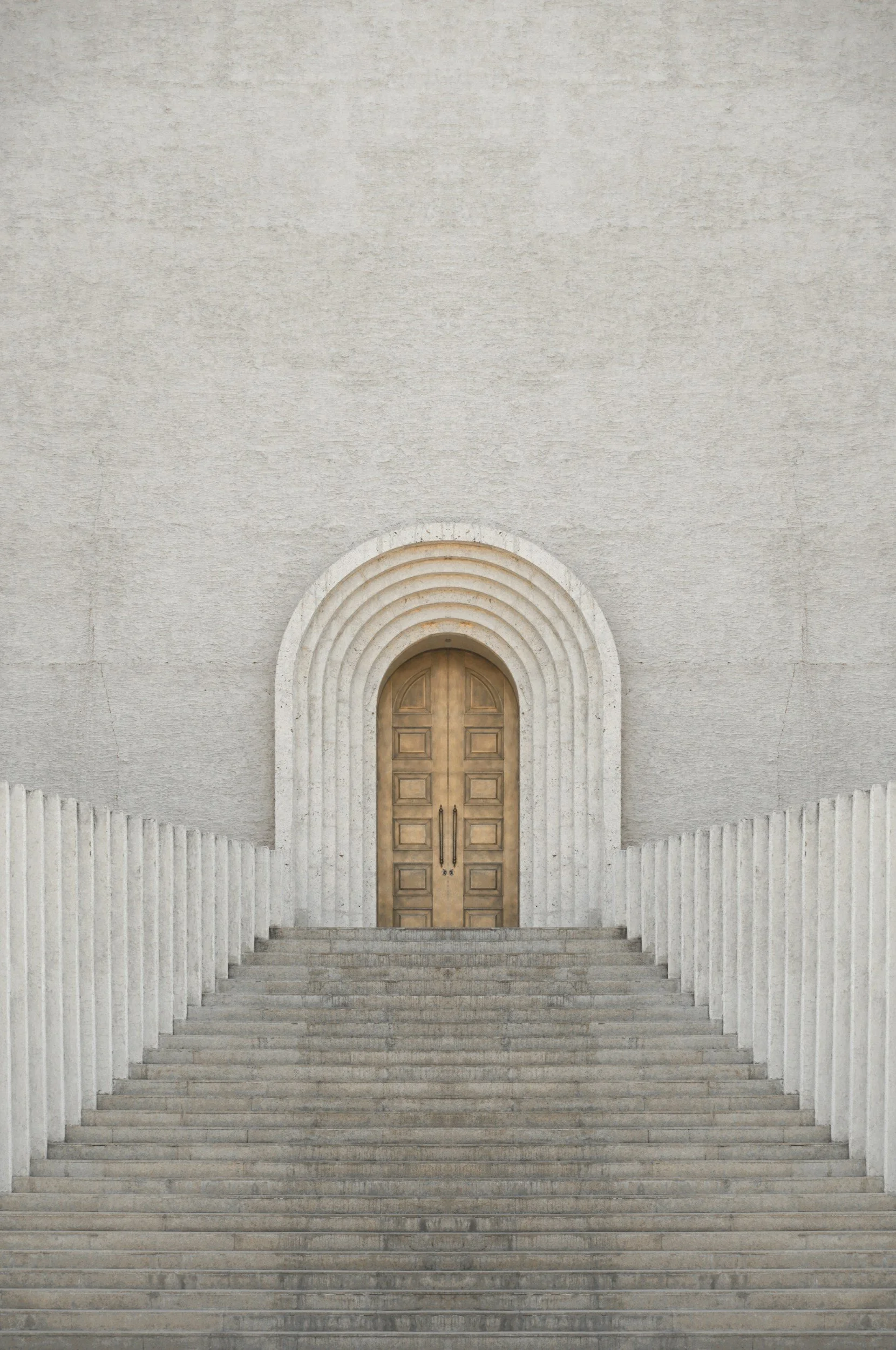 Stone staircase leading to a large wooden door framed by a semicircular arch with concentric stone details. The wall surrounding the door is plain and textured.