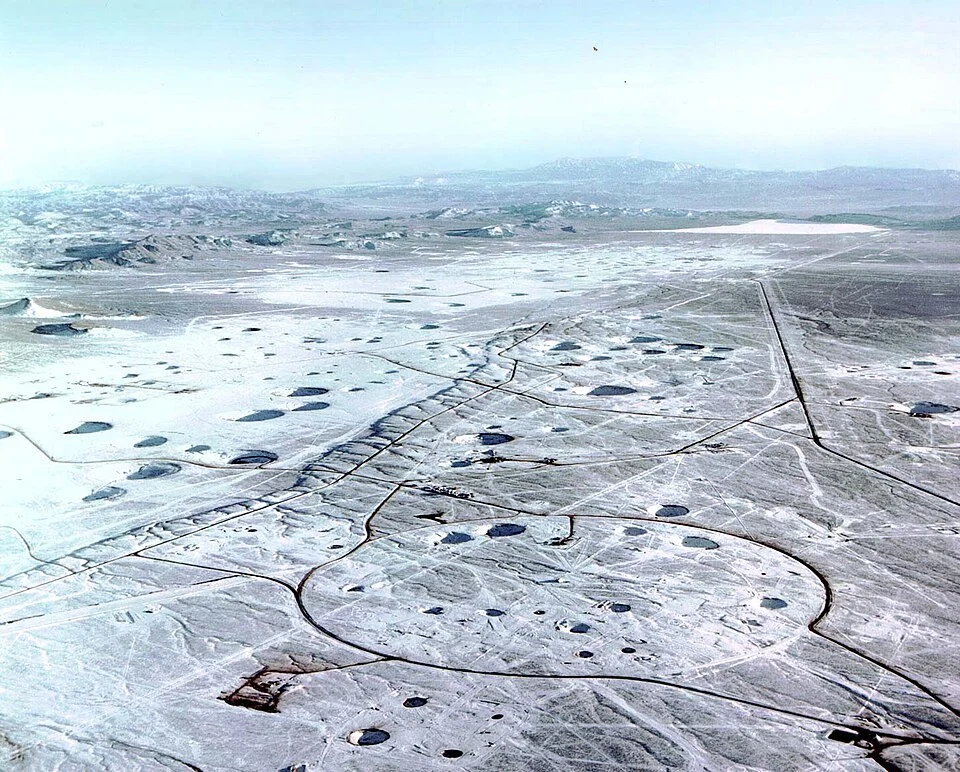 Aerial view of a snow-covered landscape with circular and irregularly shaped formations, roads, and a distant mountain range.