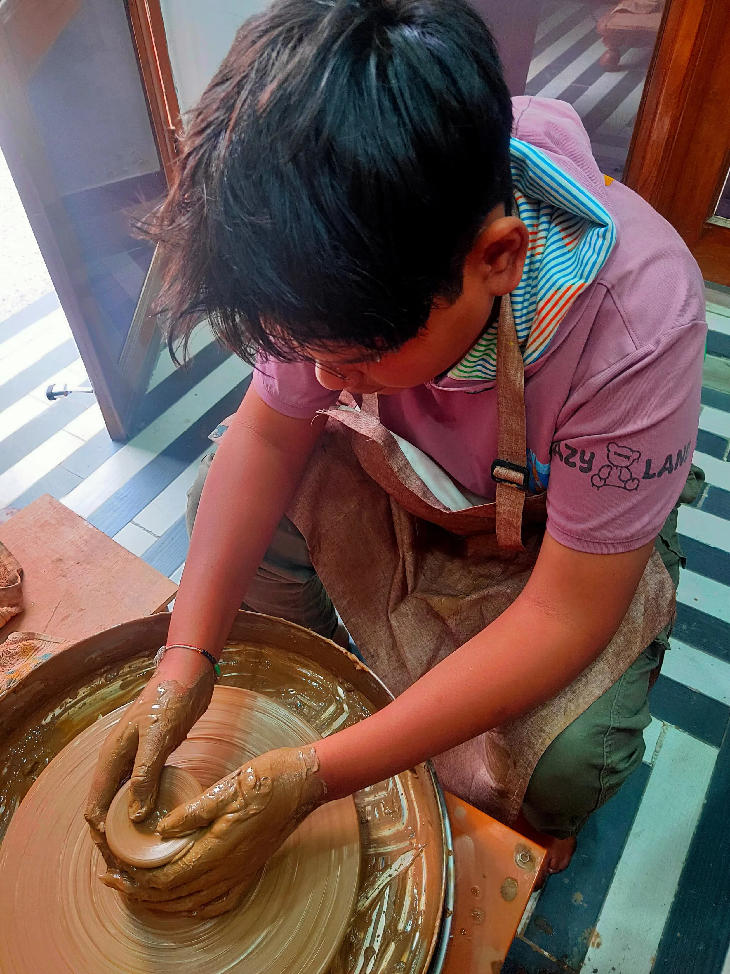 A person shaping a clay on a pottery wheel in a studio or workshop, with focus on hands and wheel.