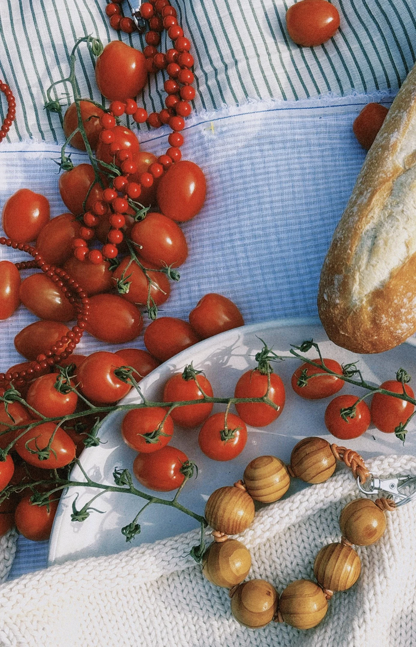 Tomatoes, cherry tomatoes, garlic, onions, bread, and a knitted cloth on a table.