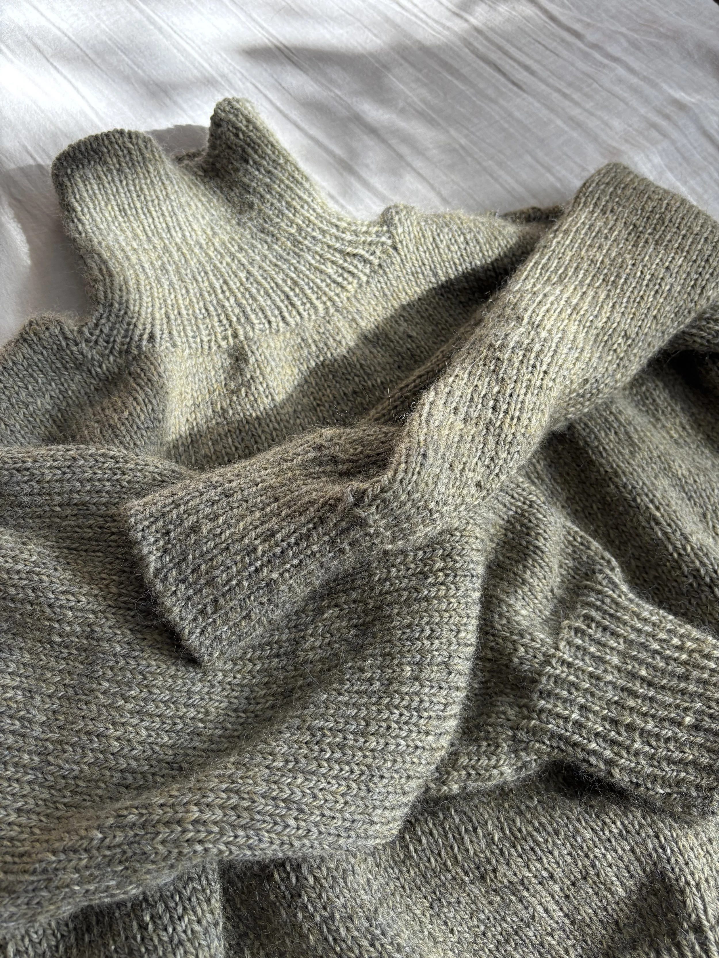 Close-up of a pair of gray knitted gloves resting on a gray knitted sweater.