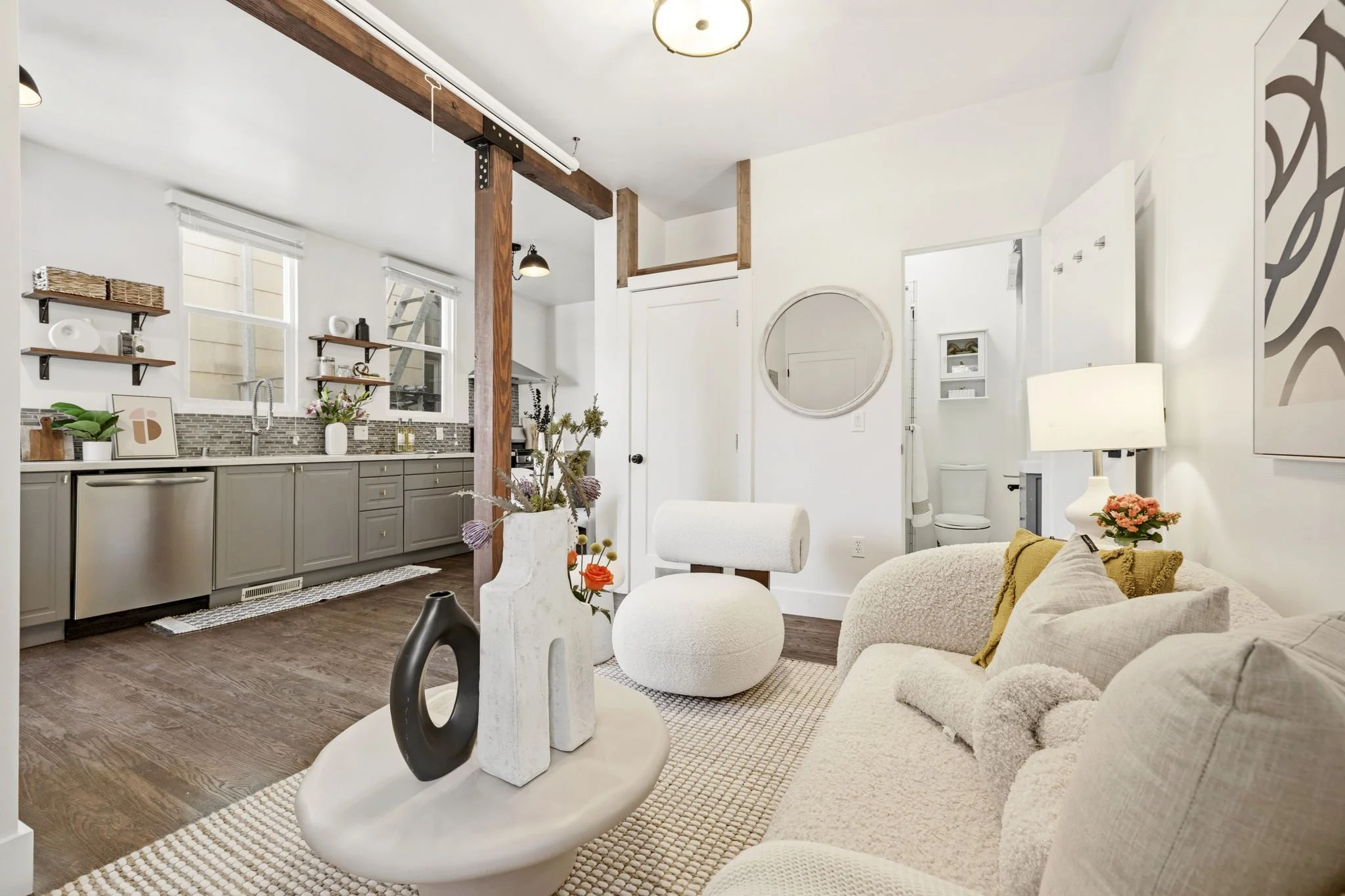 Open-concept living room and kitchen with neutral color scheme, decorated with modern furniture, pottery, and plants.