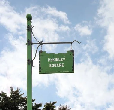 Street sign reading "McKinley Square" hanging from a green pole against a partly cloudy sky.