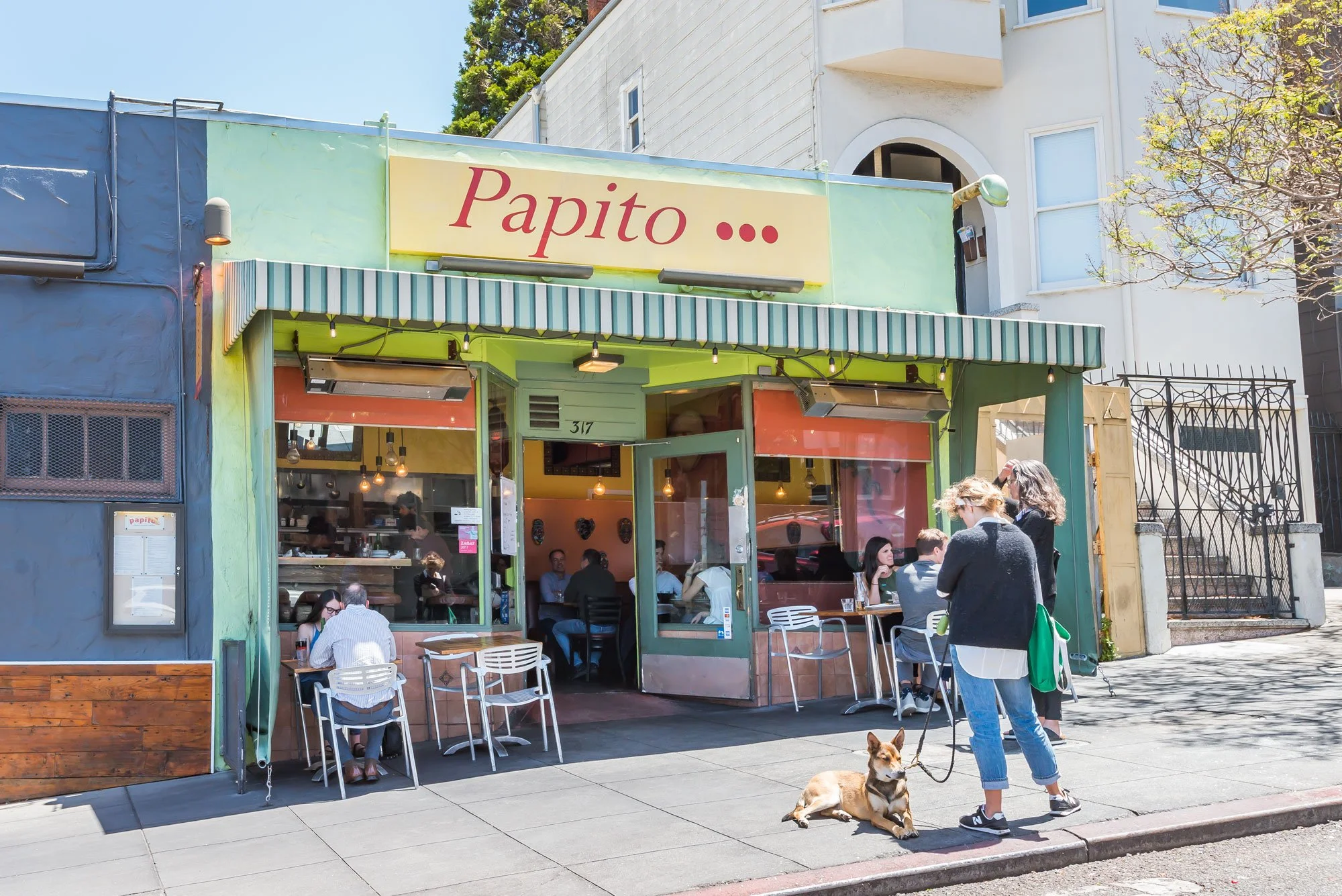 People dining outside a restaurant with a sign reading "Papito" on a sunny day.