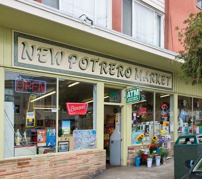 Exterior of a New Potrero Market storefront with signs for ATM and Open, displaying various products and decorations outside.