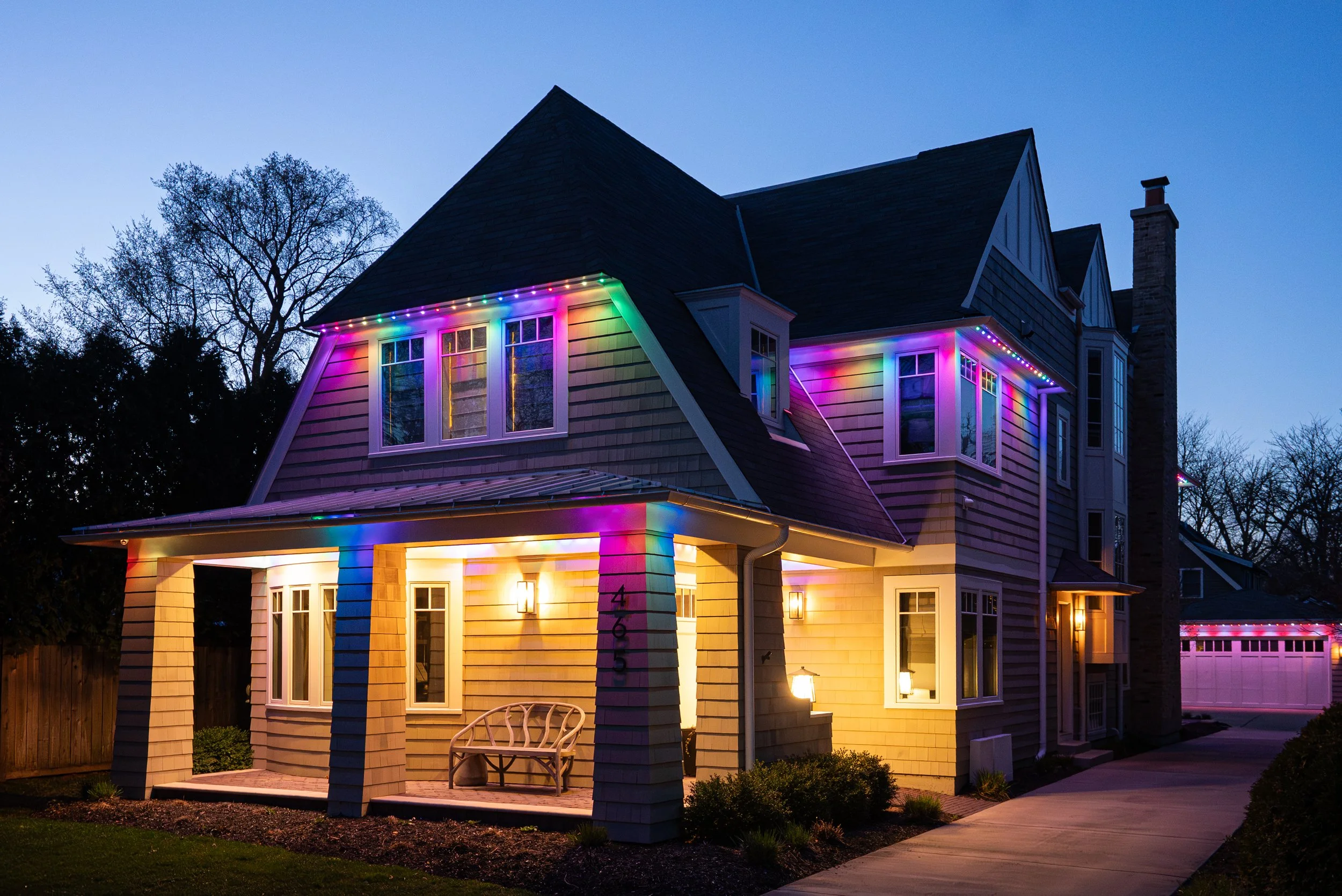 A house decorated with colorful string lights at dusk, illuminating the exterior and surrounding trees.