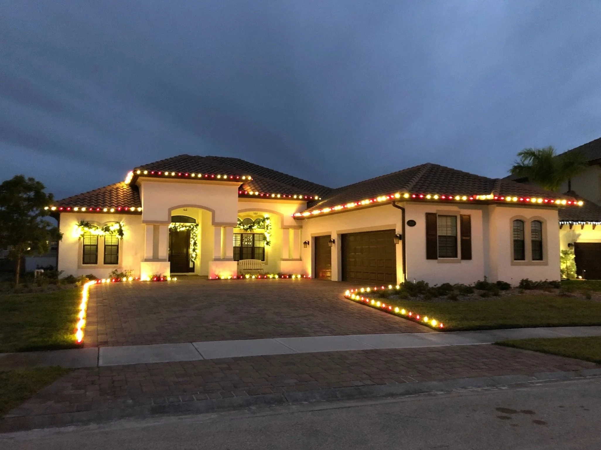 A house decorated with string lights along the roofline and around the doorway, illuminated at dusk or night.