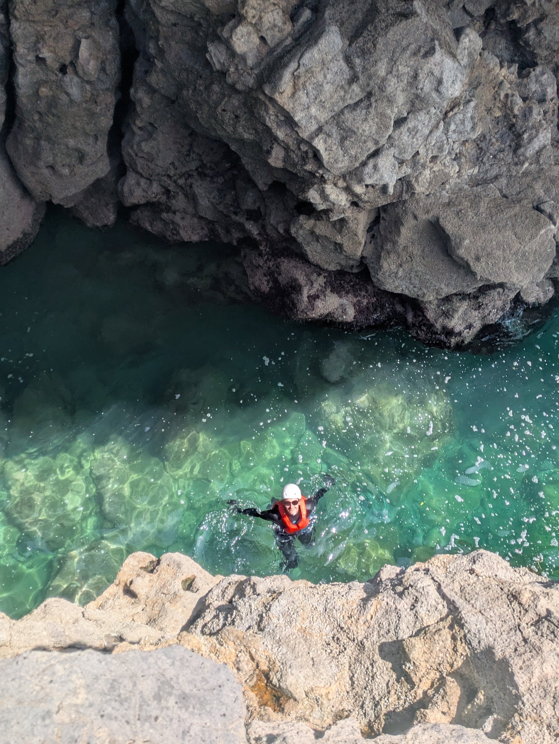 A person in water near rocky terrain, wearing a helmet and life vest, smiling at the camera.